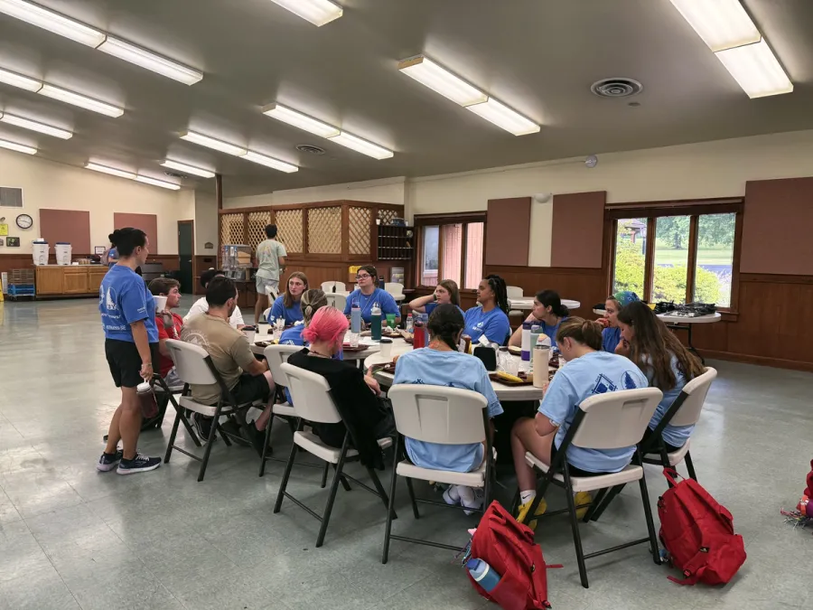 Campers in blue camp shirts eat and talk around a round table in the dining hall.