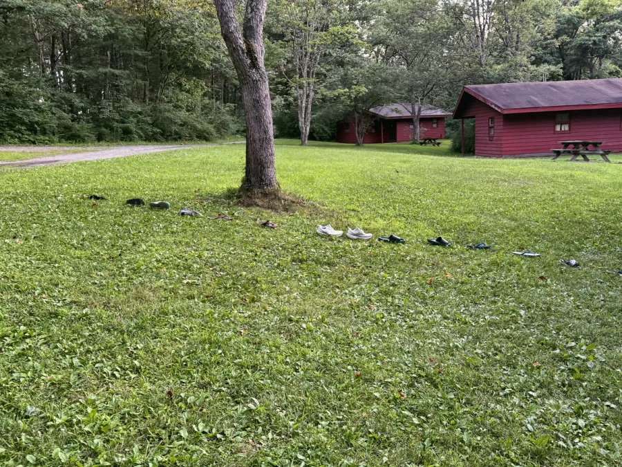 Shoes and sandals lined up on the grass in front of two red cabins