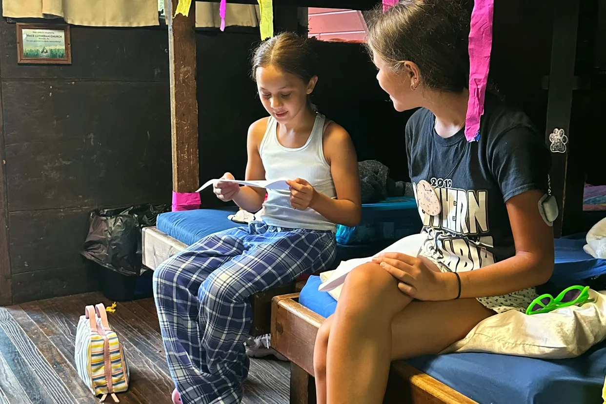 Two girls sit on a bunk bed in a rustic cabin decorated with ribbons
