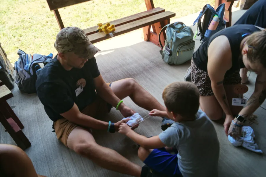 A man helps a young boy with a craft project on a cabin porch