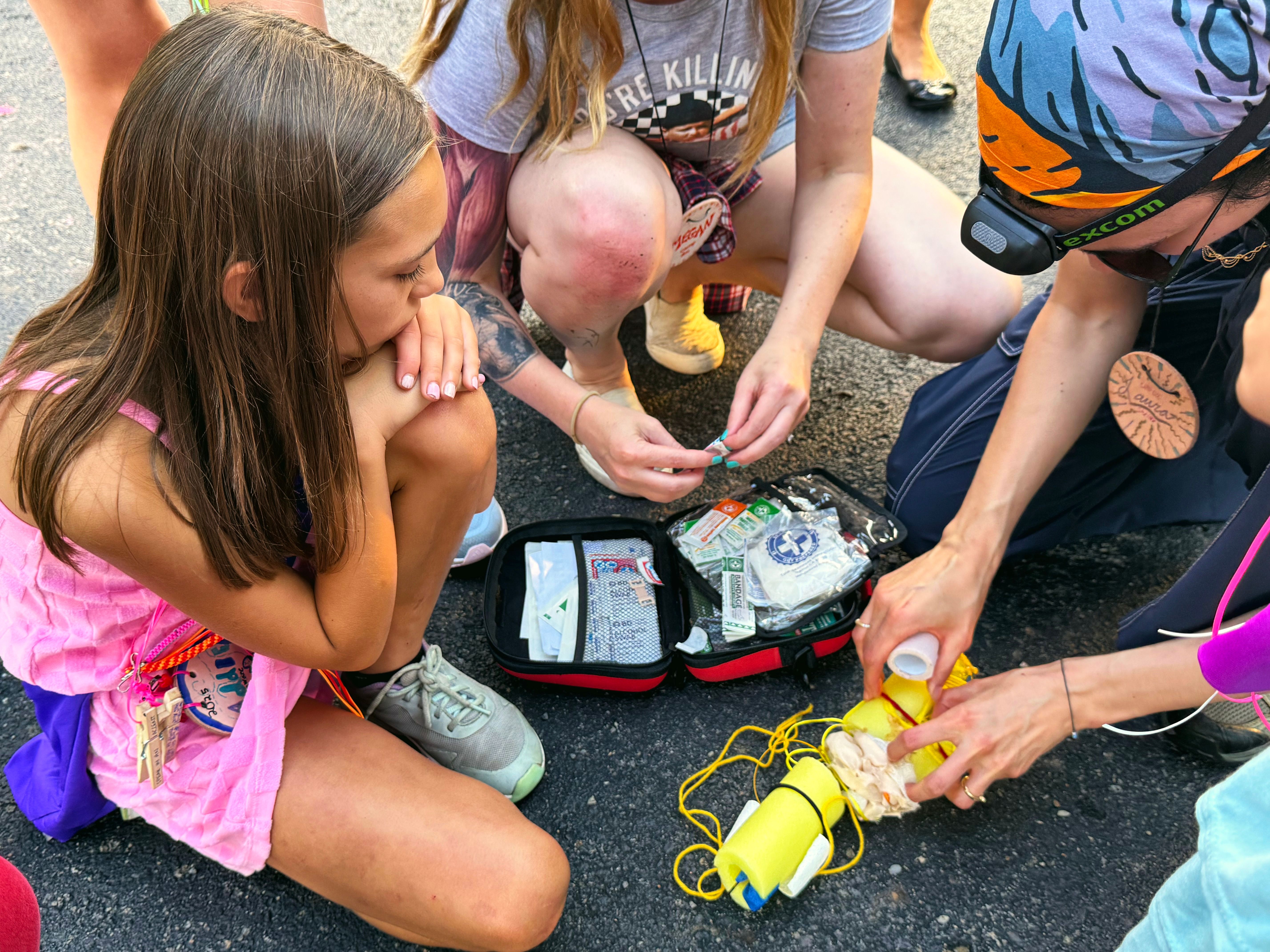 Camp staff kneel beside an open first-aid kit and show a young camper how to wrap a splint.