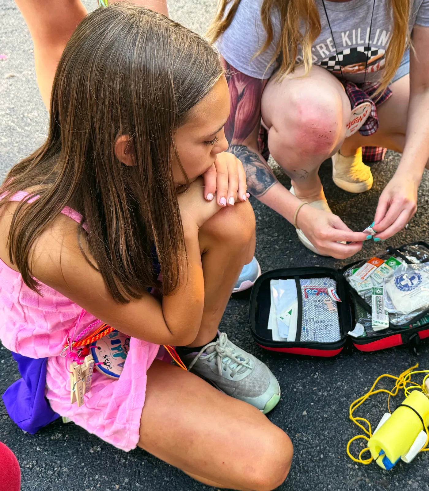 Camp staff open a first-aid kit on the ground while a young camper watches.