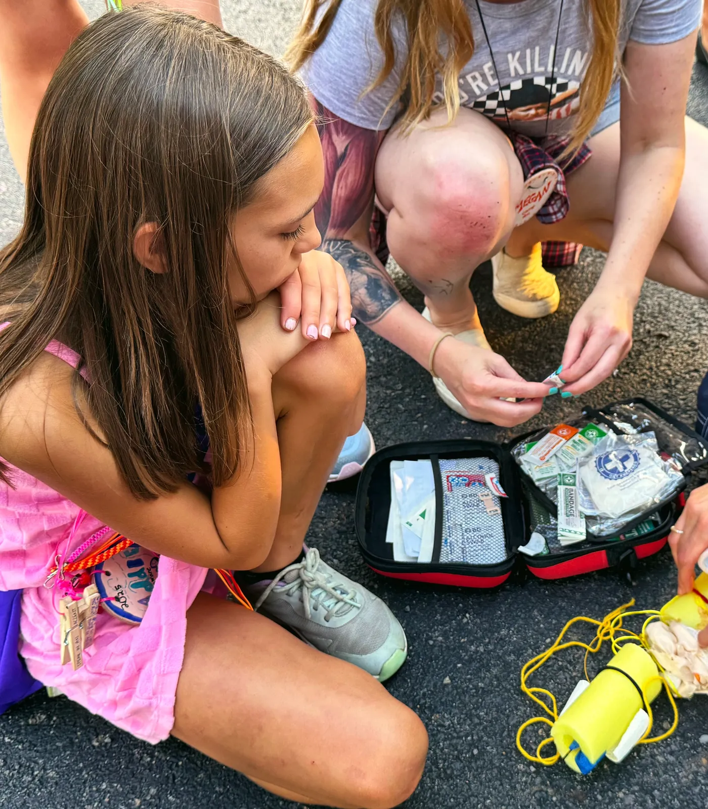 Camp staff kneel beside an open first-aid kit and show a young camper how to wrap a splint.