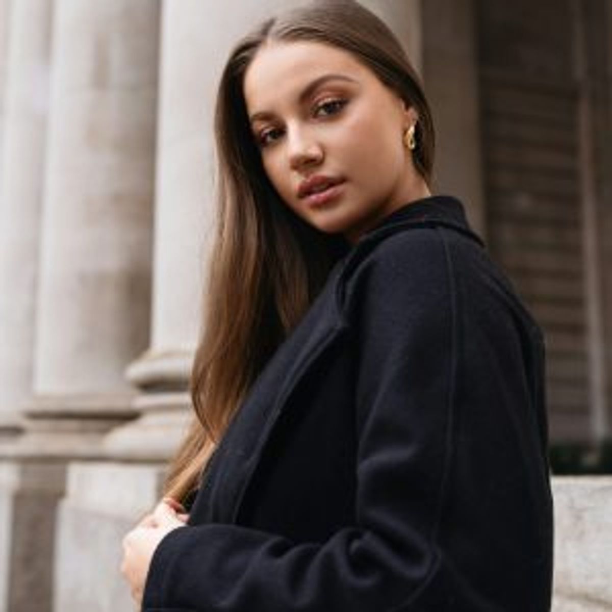 Young woman in a black outfit standing beside stone columns
