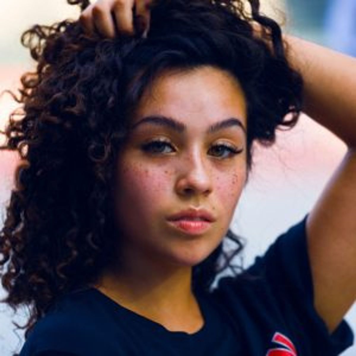 Woman with curly hair resting her hands on her head