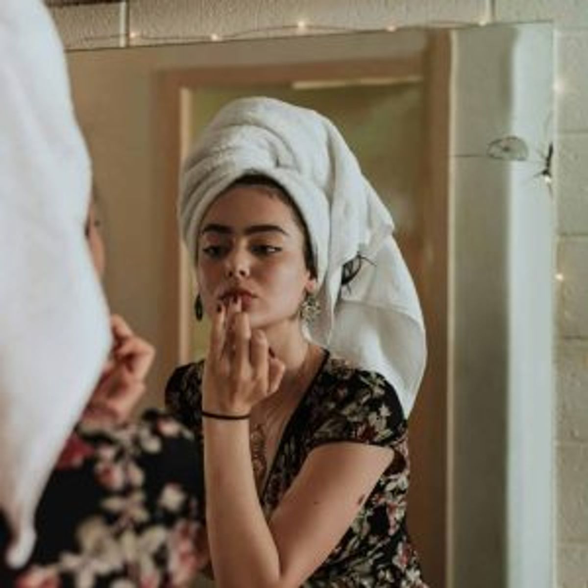 Woman in a hair towel applying lip colour in a mirror