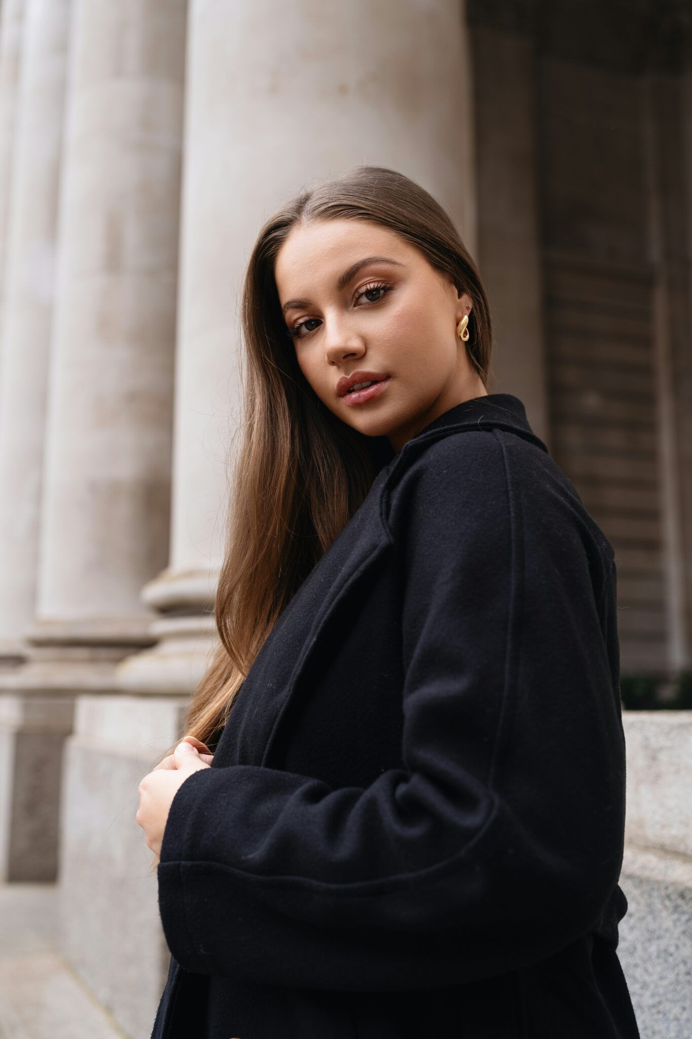 Woman in a black coat standing beside stone columns