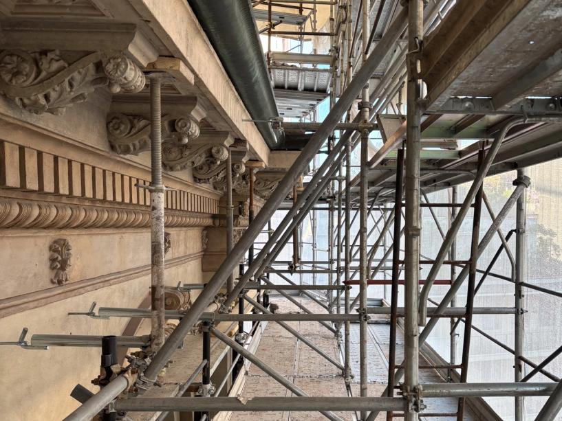 I cornicioni decorati della facciata visti da vicino, dietro i ponteggi del cantiere