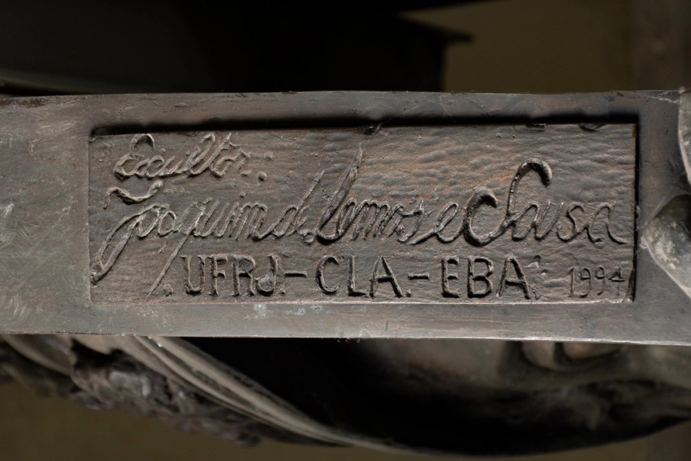 Uma assinatura de Joaquim de Lemos e Souza estilizada em preto, escrita em traços cursivos, que está localizada no medalhão da UFRJ