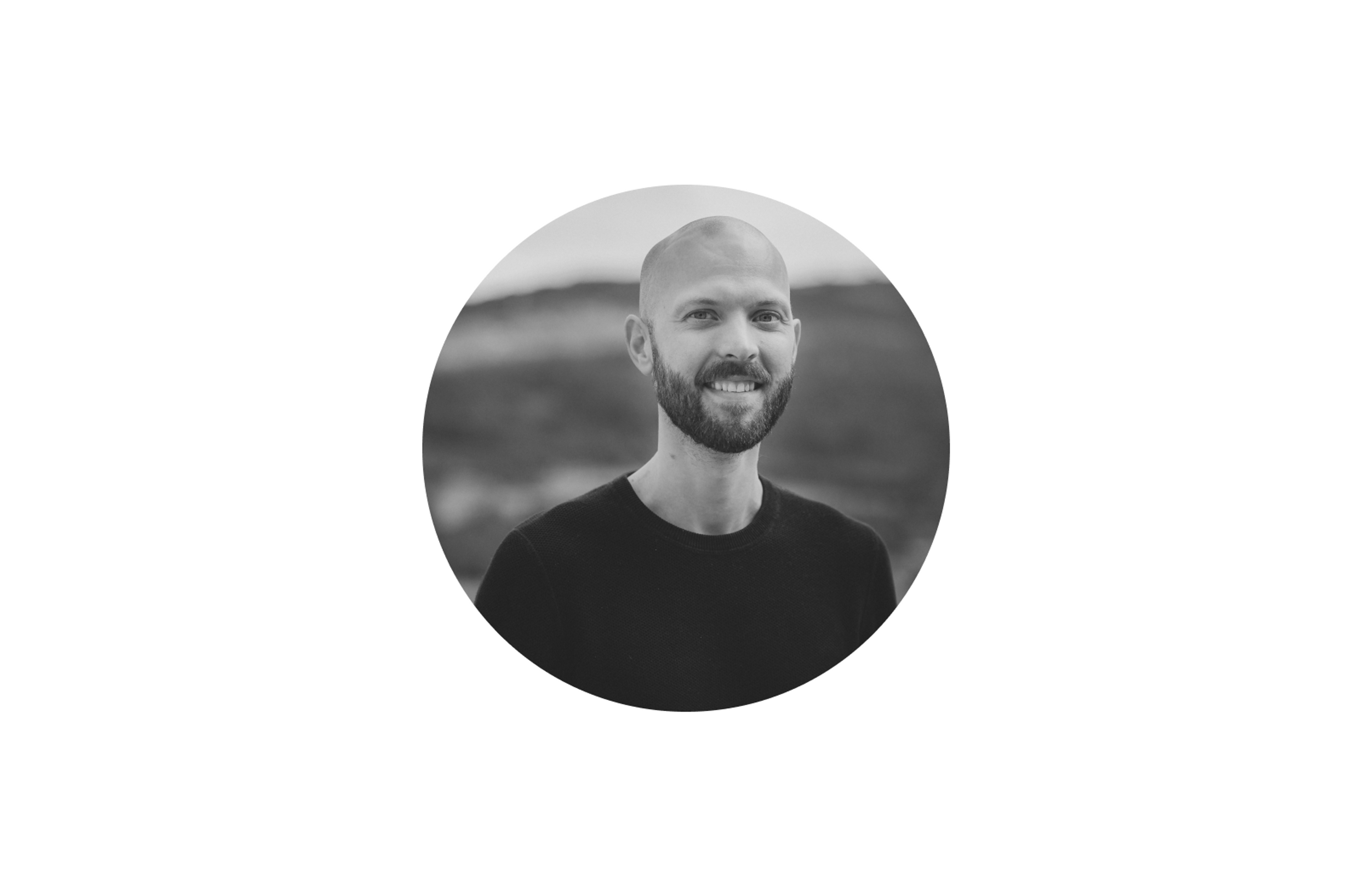 Svart/hvitt-bilde av mann med tåkete bakgrunn. Ser inn i kamera og smiler.