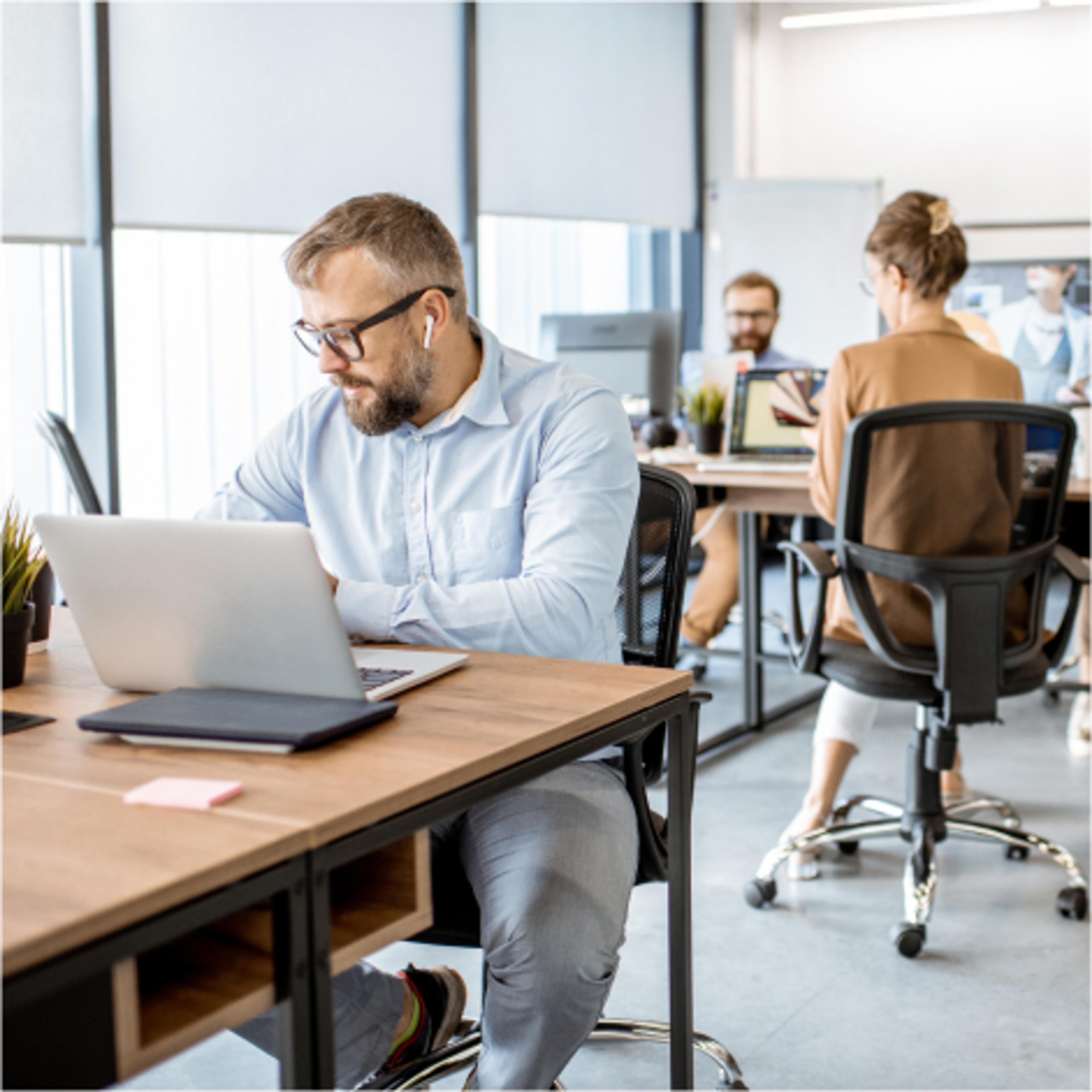 Konsulent som sitter i åpent landskap med to kollegaer i bakgrunnen