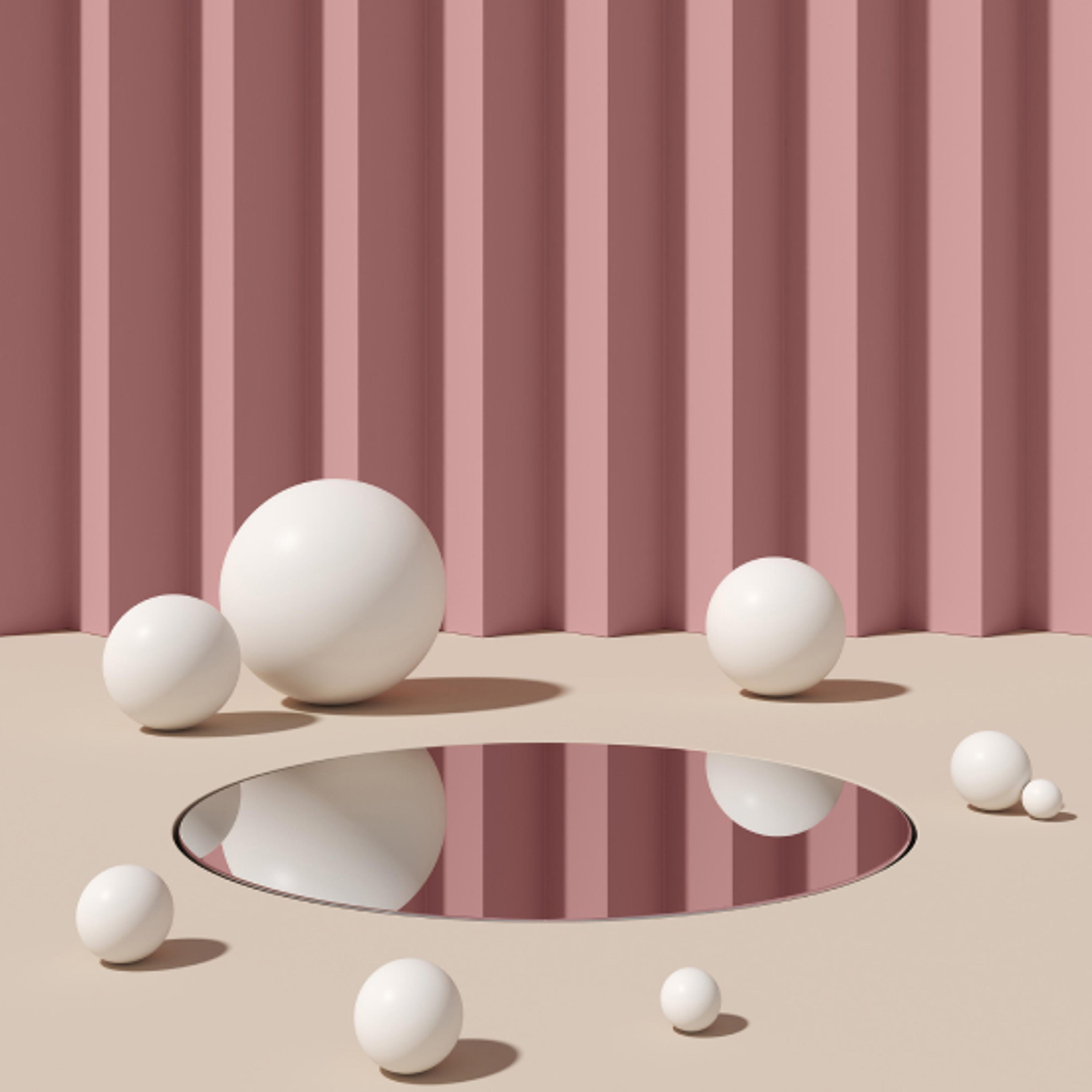 Hvite baller av ulik størrelse som ligger på et gulv med et hull i midten. Ruglete vegg i rosa i bakgrunn.