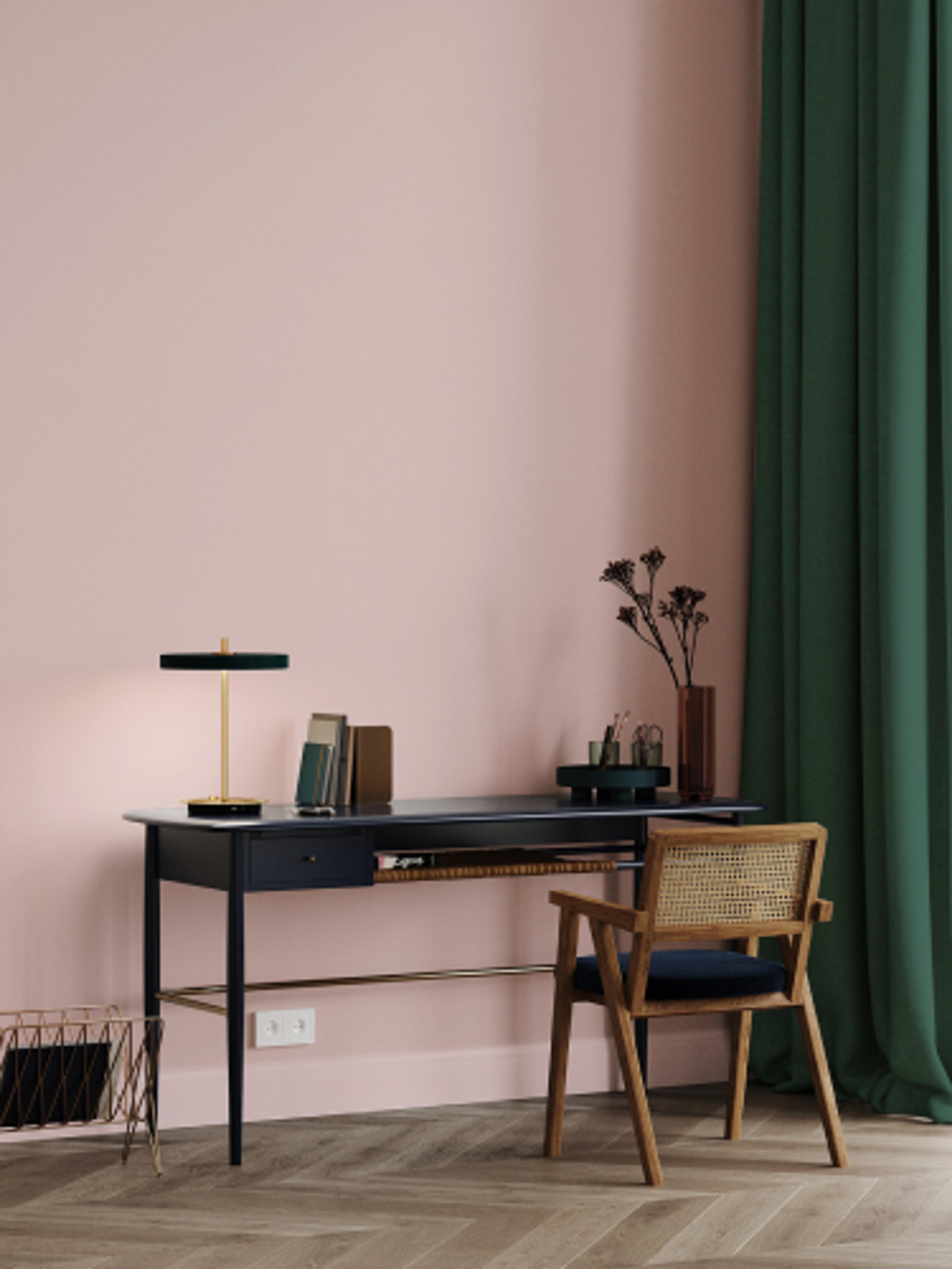 En stol som står forran et skrivebord i et rosa rom, med en lang grønn gardin forran vinduet..