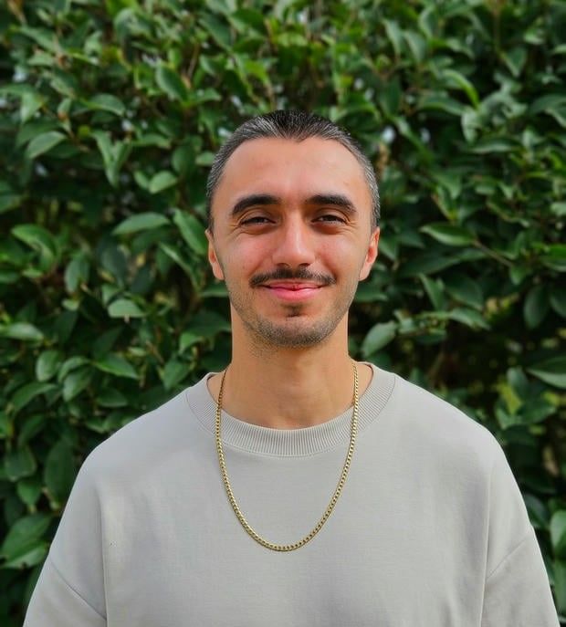 Lucian Chevallier, founder of Lumin web design, development & strategy, stood outside in front of a green leafy background.