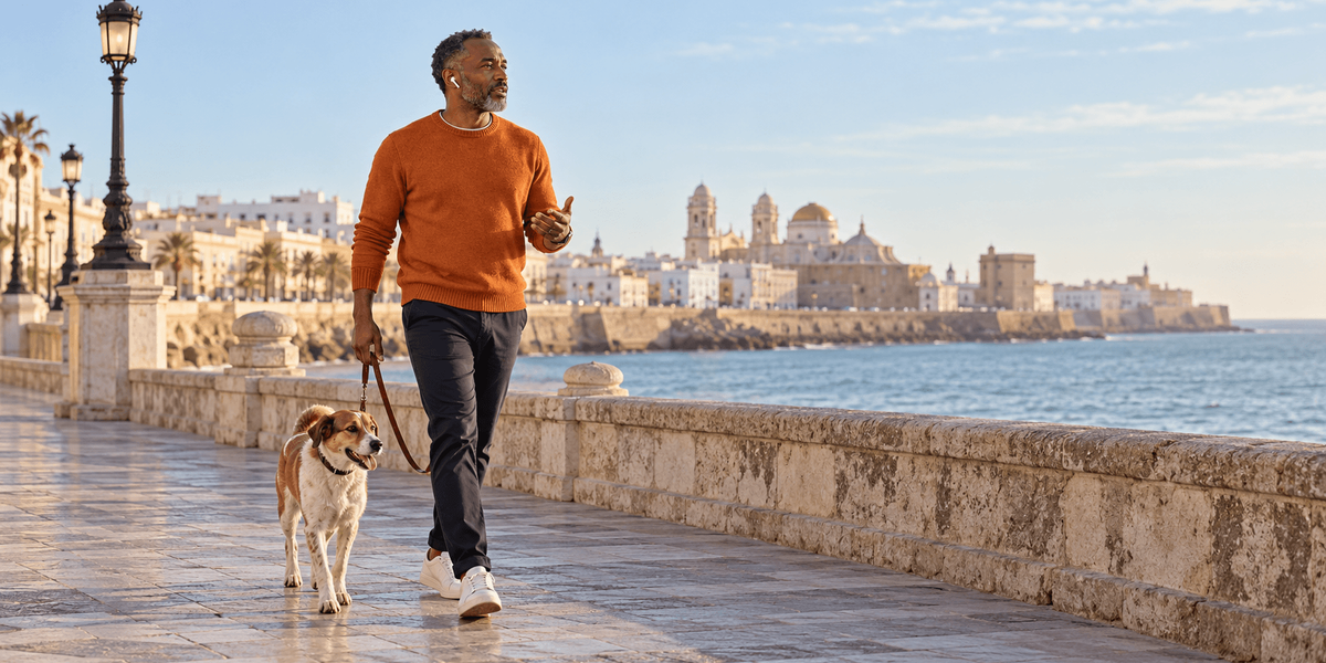Propietario de una empresa de EE. UU. paseando a su perro por el paseo marítimo de Cádiz mientras habla con su equipo, dirigiendo su LLC desde España con la Visa de Nómada Digital