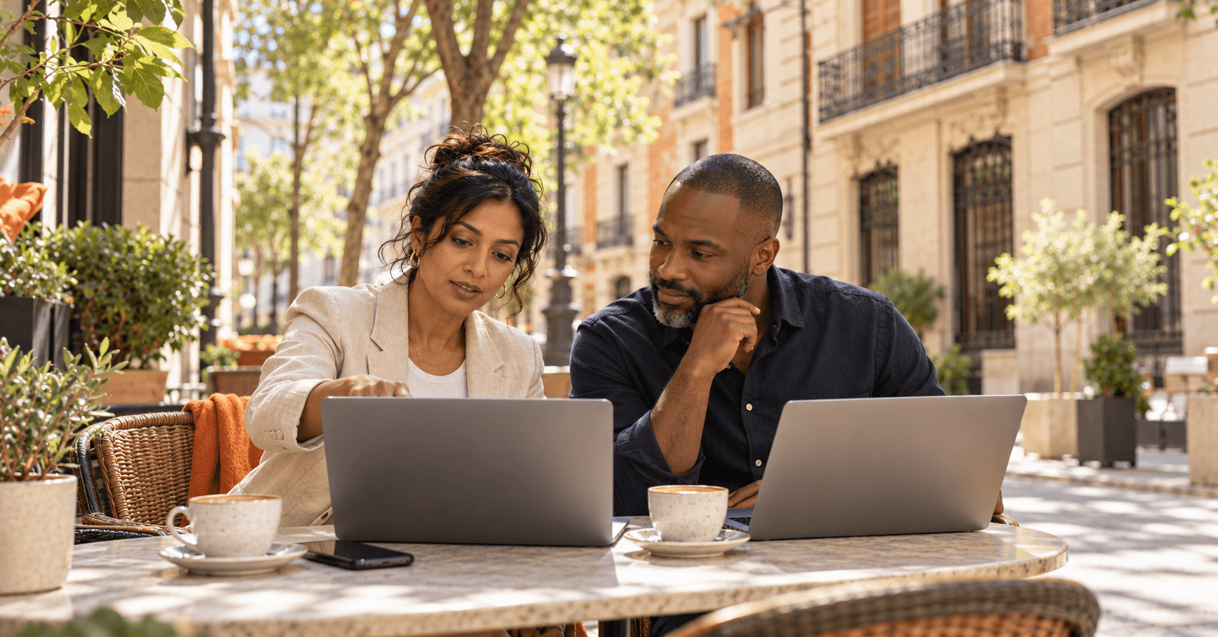 Two business partners working on their laptops at a café terrace in Madrid, deciding their Spain Digital Nomad Visa route as company owners