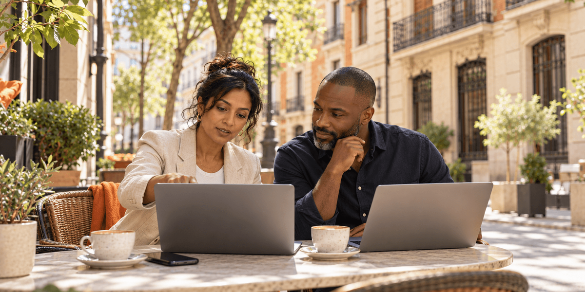 Two business partners working on their laptops at a café terrace in Madrid, deciding their Spain Digital Nomad Visa route as company owners