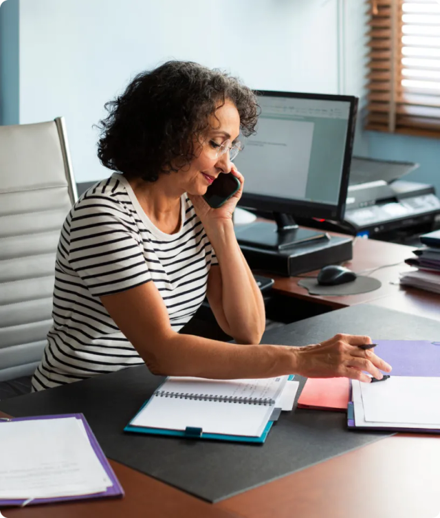 A woman seated at a desk, engaged in a conversation on the phone.