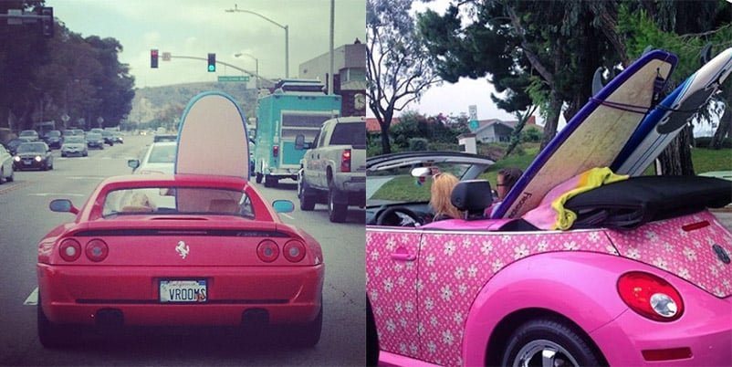 Two convertibles, one red and one pink with a flower pattern, carry surfboards upright in their seats.