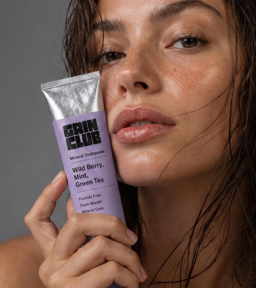 A model with wet hair holding a Grin Club tube against her cheek.
