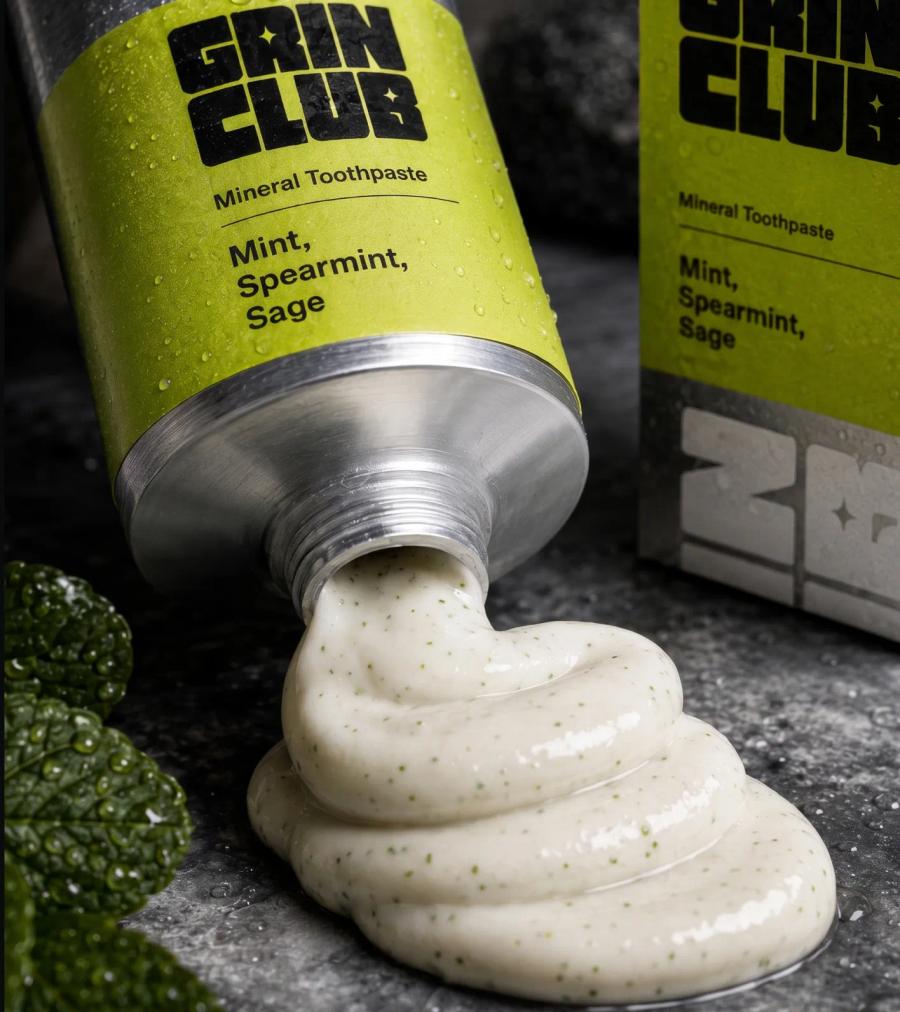 A Grin Club tube on its side with mineral paste squeezed out beside the carton.
