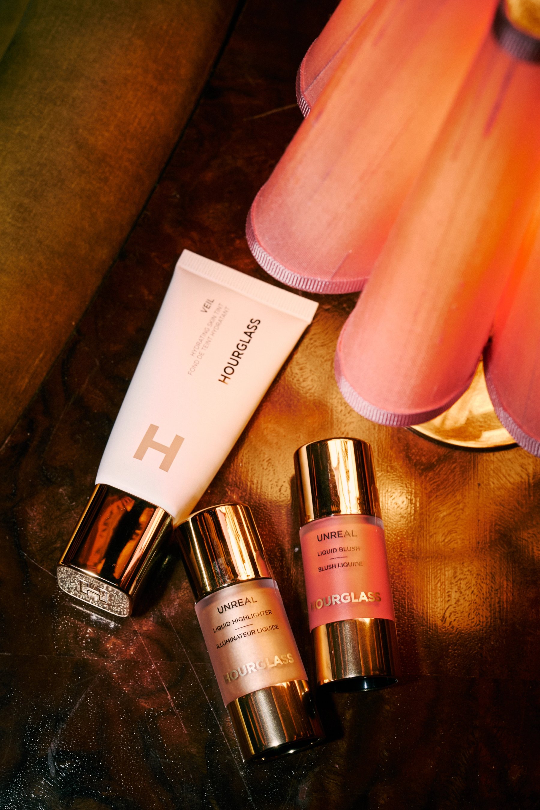 hourglass skin tint highlighter and liquid blush on a wood table and pink lampshade
