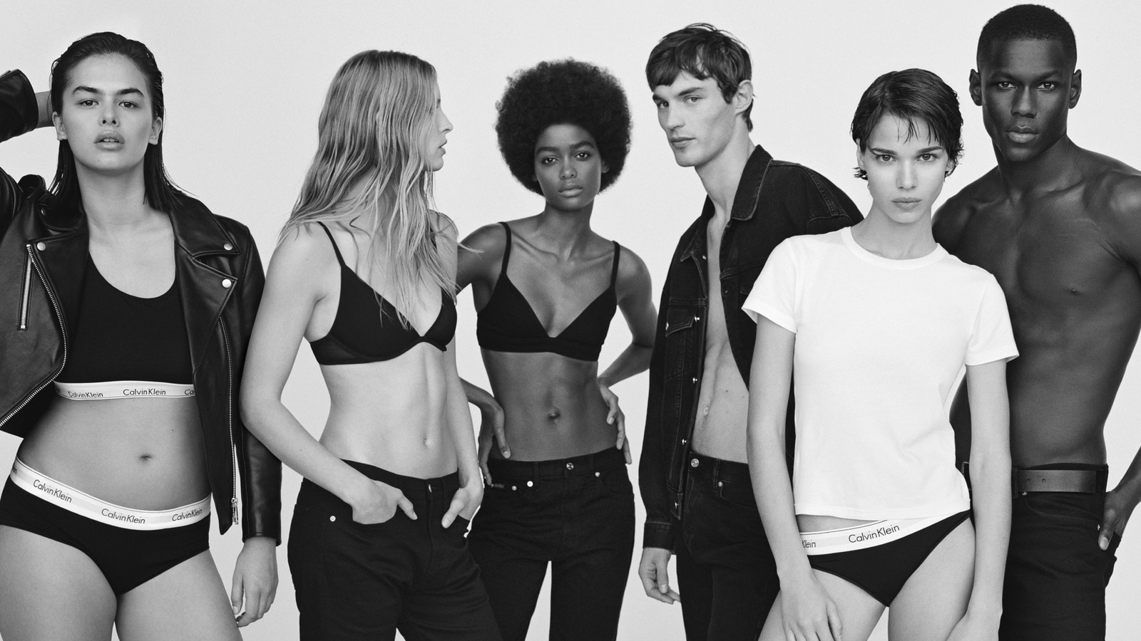 Black and white image of six diverse models in Calvin Klein underwear, posing closely. The mood is bold and edgy, with confident expressions.