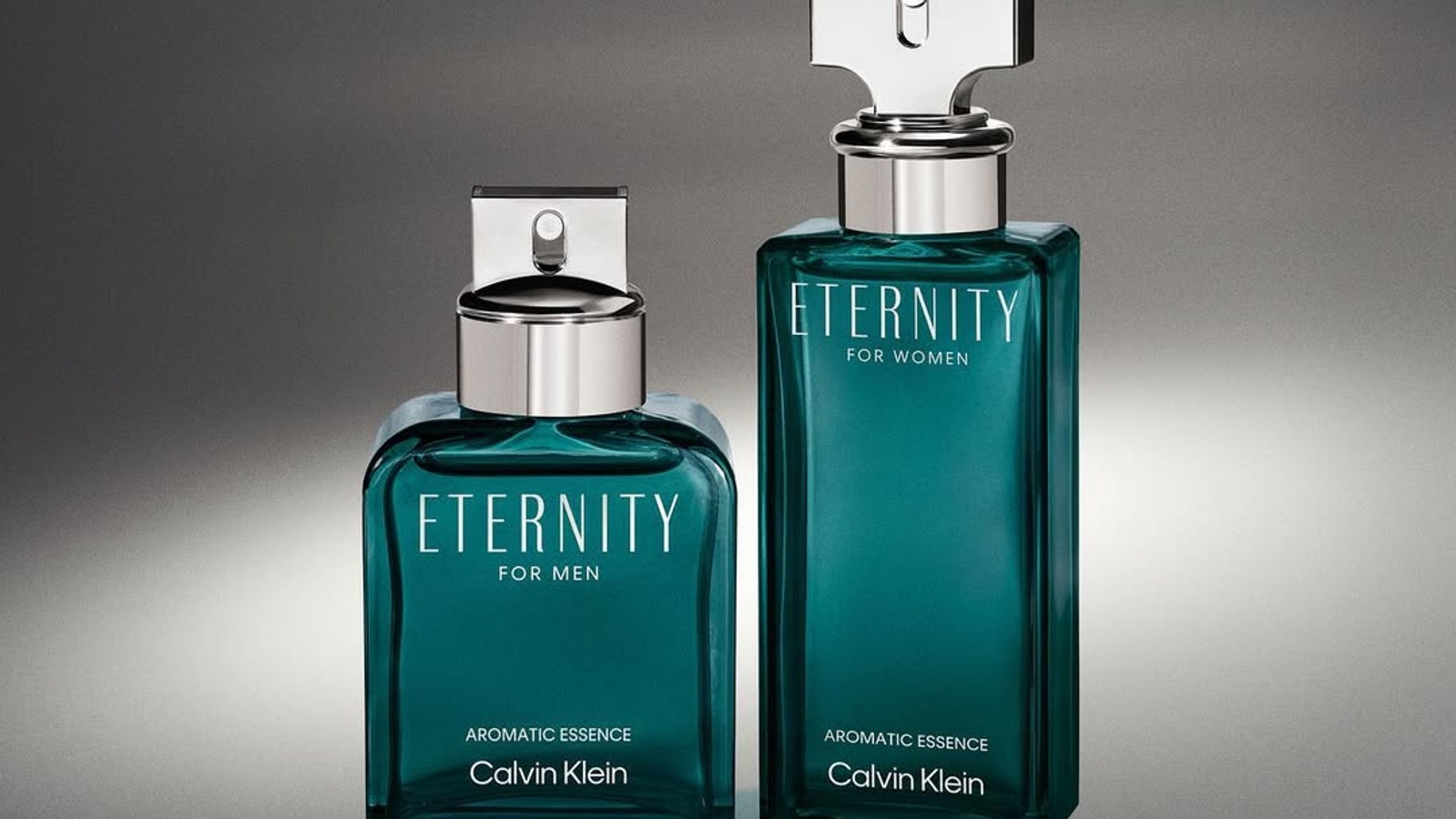 Two teal perfume bottles, "Eternity for Men" and "Eternity for Women," by Calvin Klein, stand on a reflective surface. Elegant and sophisticated presentation.