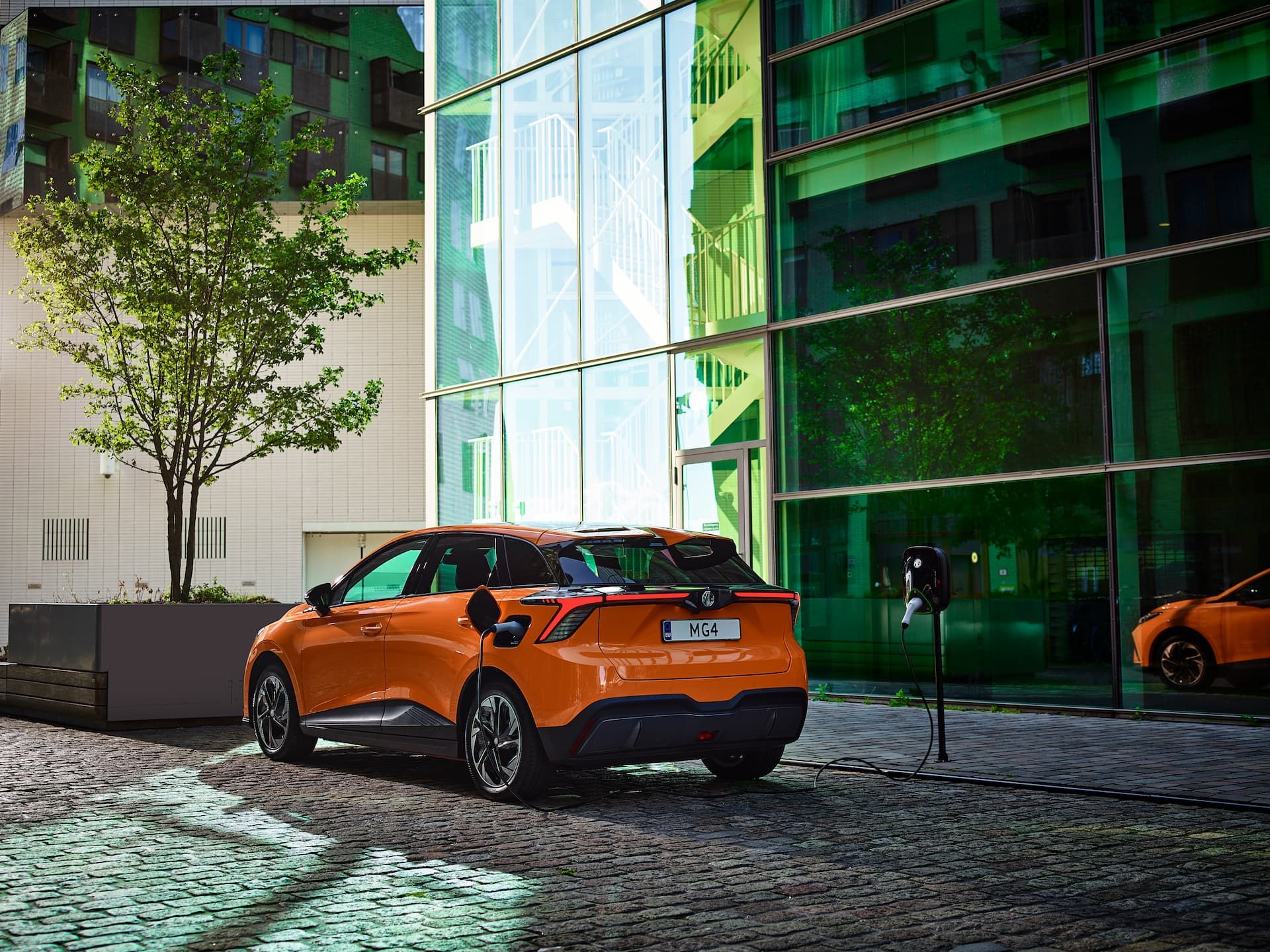 Orange MG 4 EV charging from kerbside wall box in city