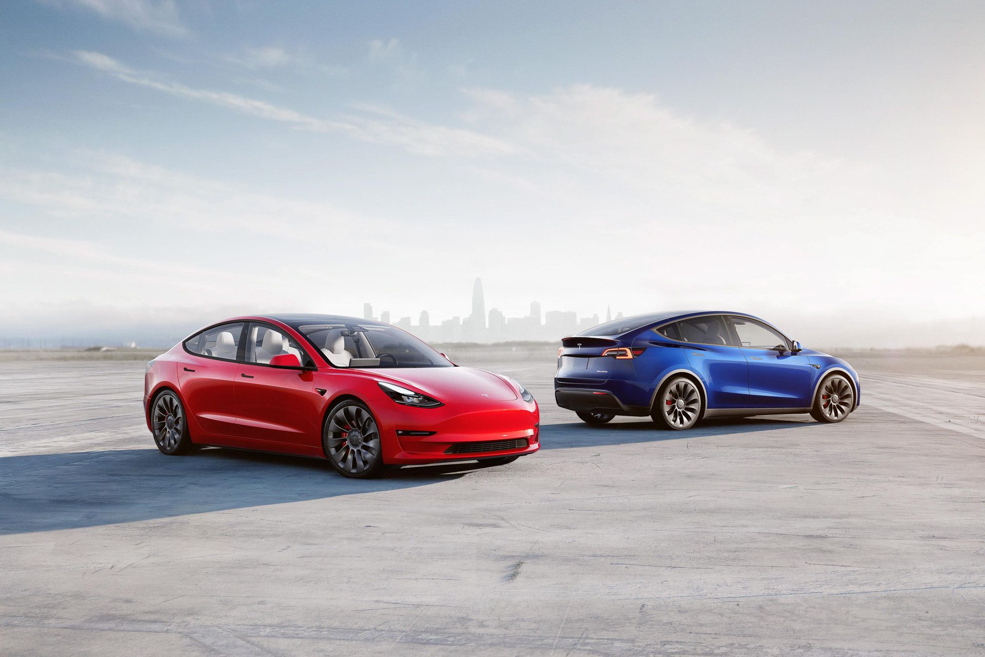Red Tesla Model 3 Performance and blue Tesla Model Y Performance in front of cityscape