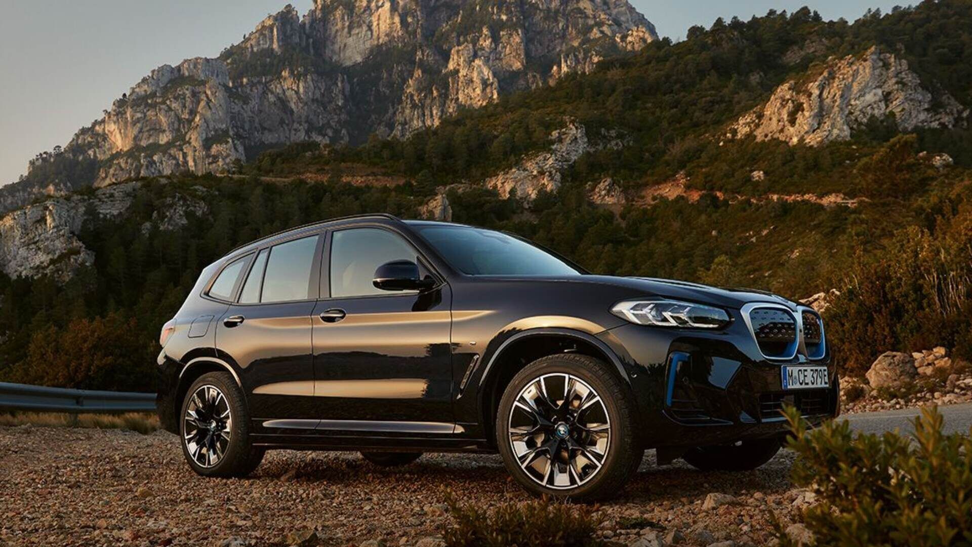 BMW iX3 driving off road with mountain background