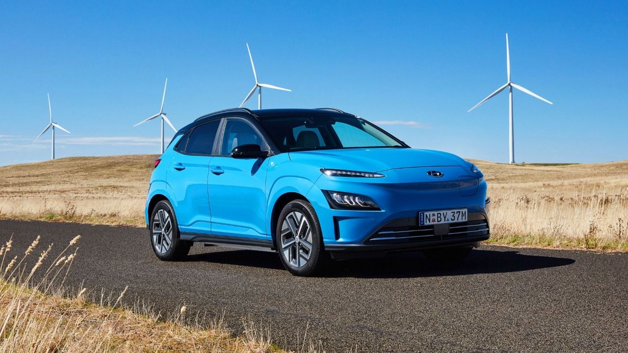 Blue and black roof Hyundai Kona Electric in front of wind turbines front view