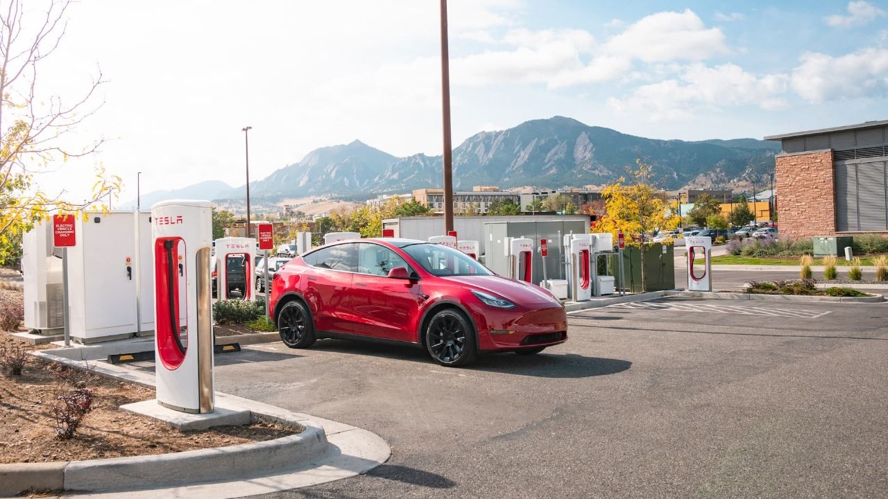 Red Tesla Model Y electric SUV charging at Supercharging station