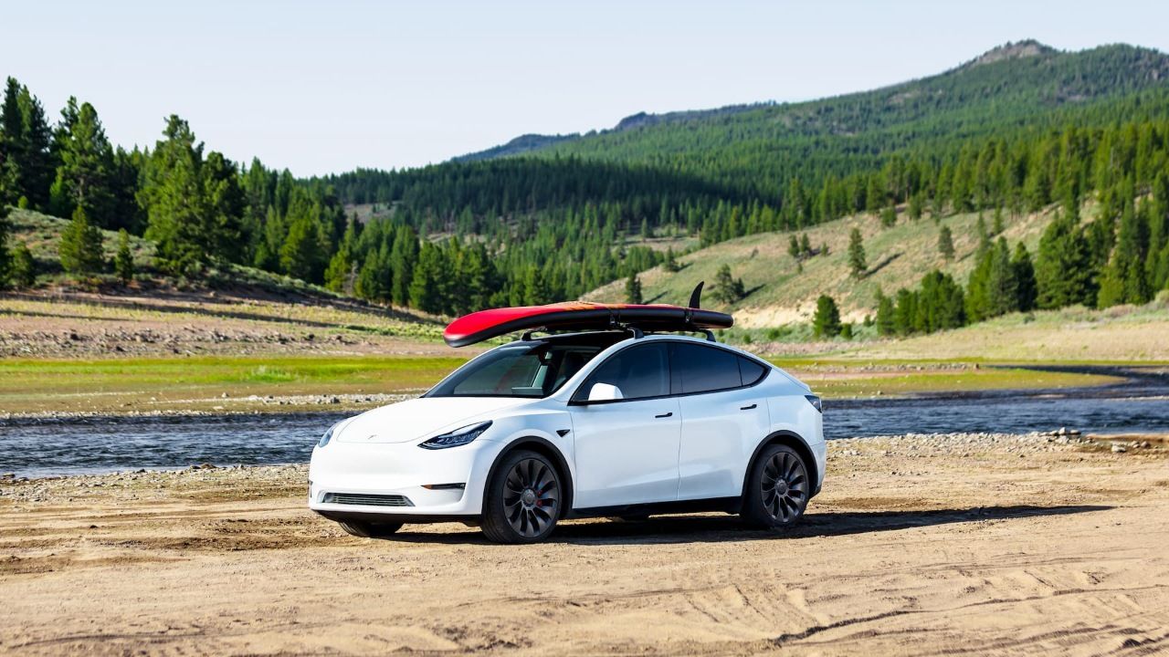 White Tesla Model Y Performance with red surfboard on roof at mountain