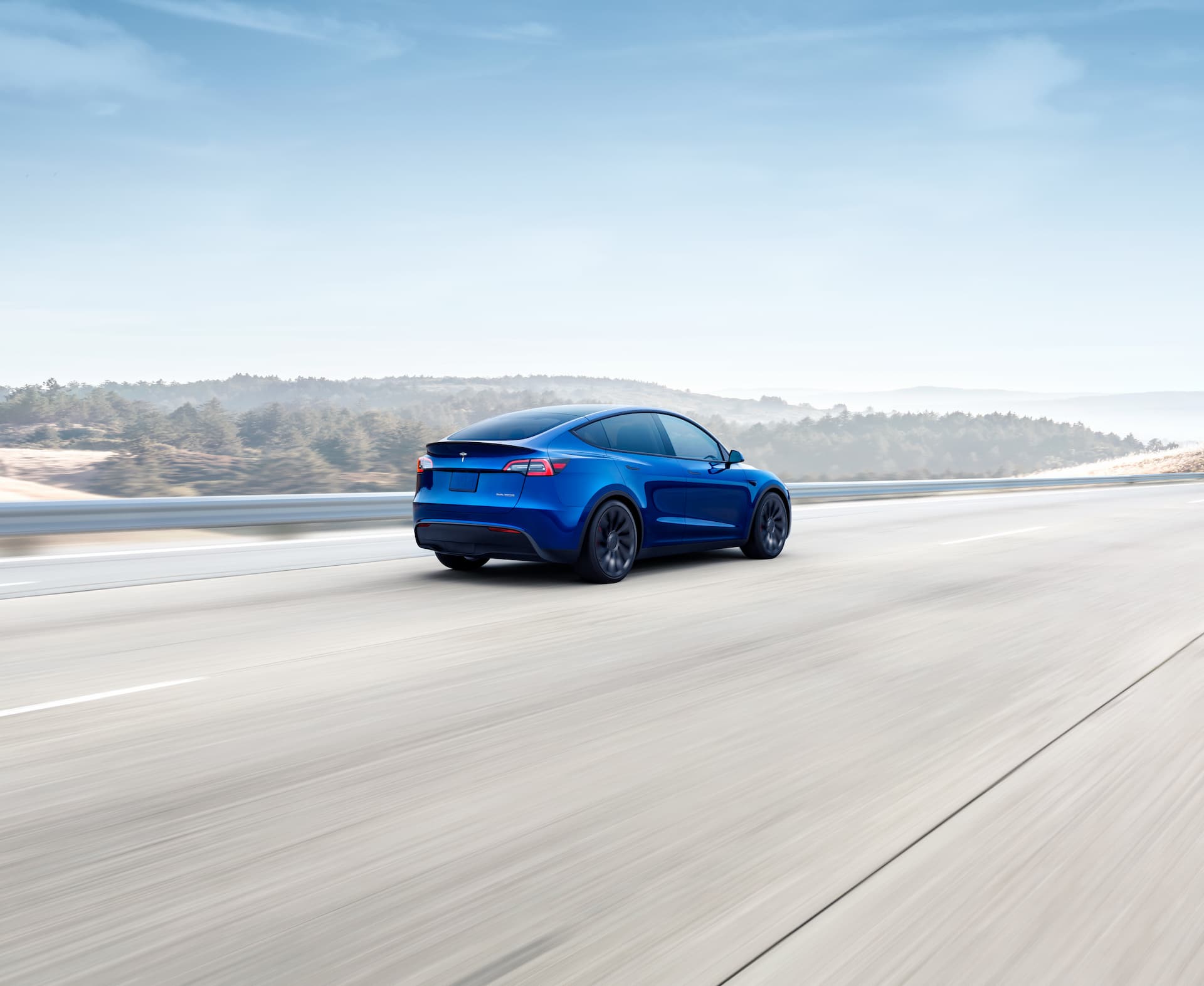 Blue Tesla Model Y driving rear view