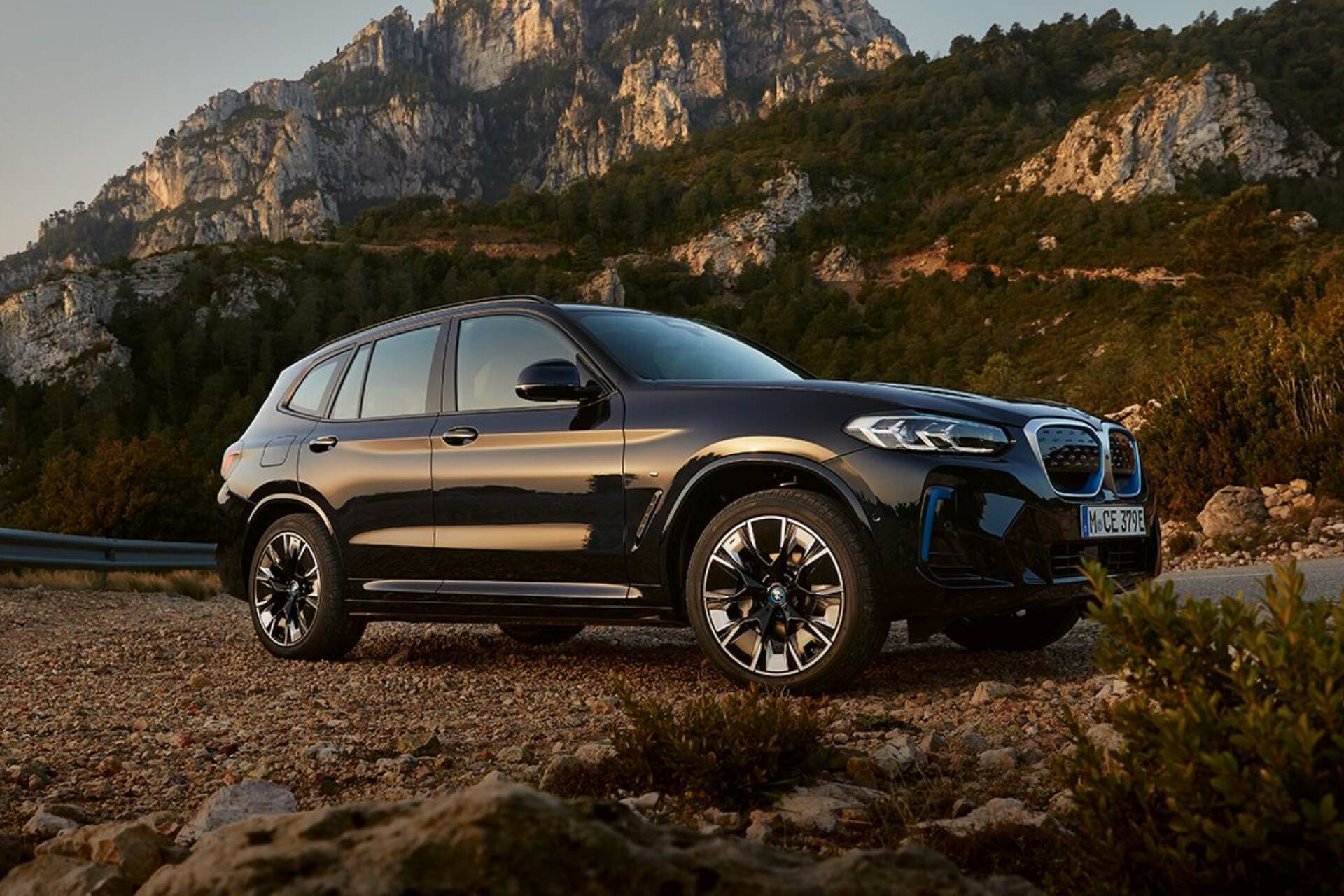 BMW iX3 side view driving off road with mountain background