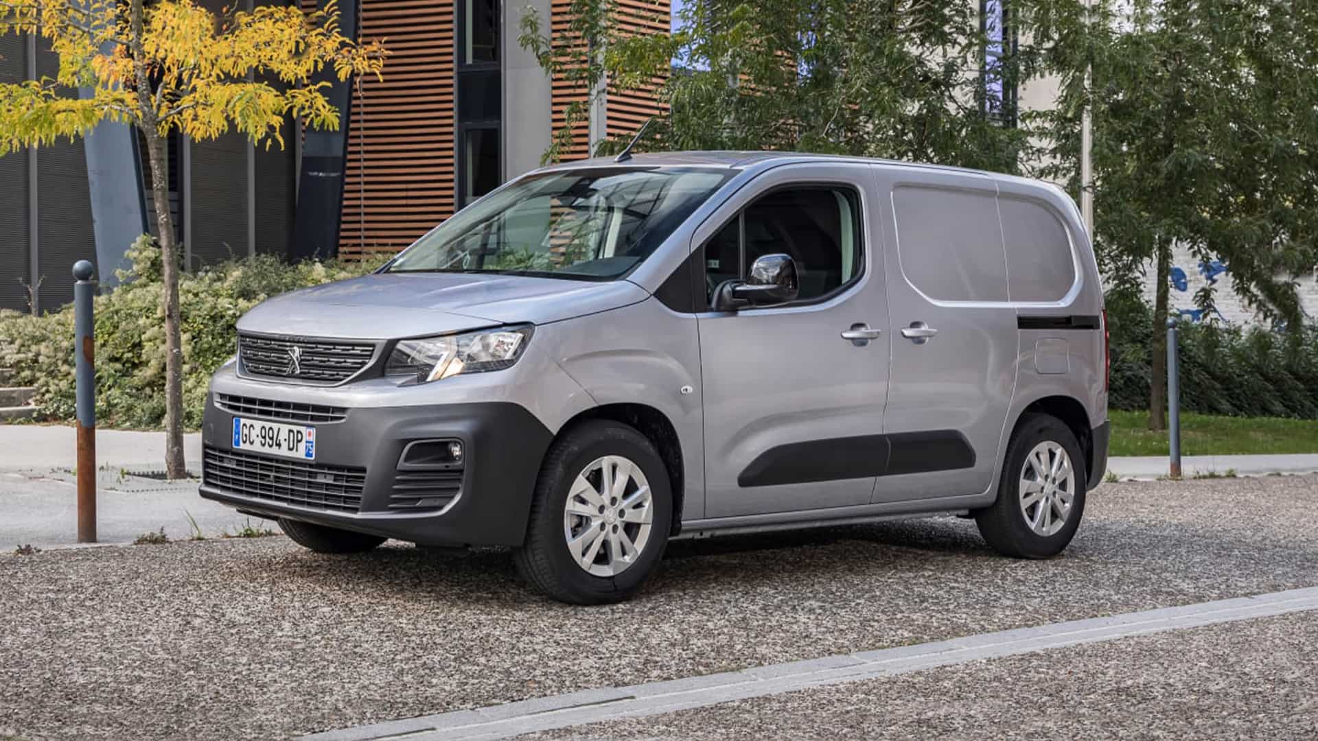 Grey Peugeot e-Partner in gravel parking lot in front of building