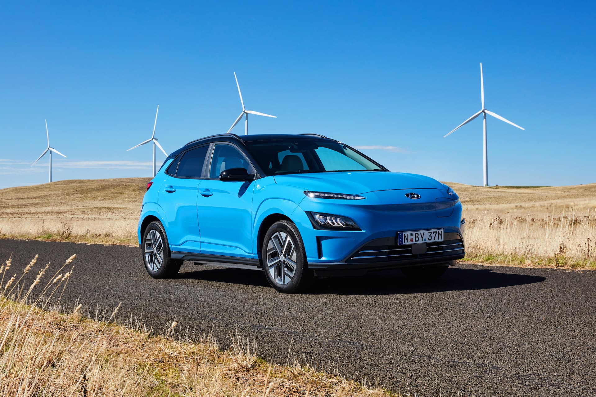 Blue Hyundai Kona Electric SUV in front of windmills