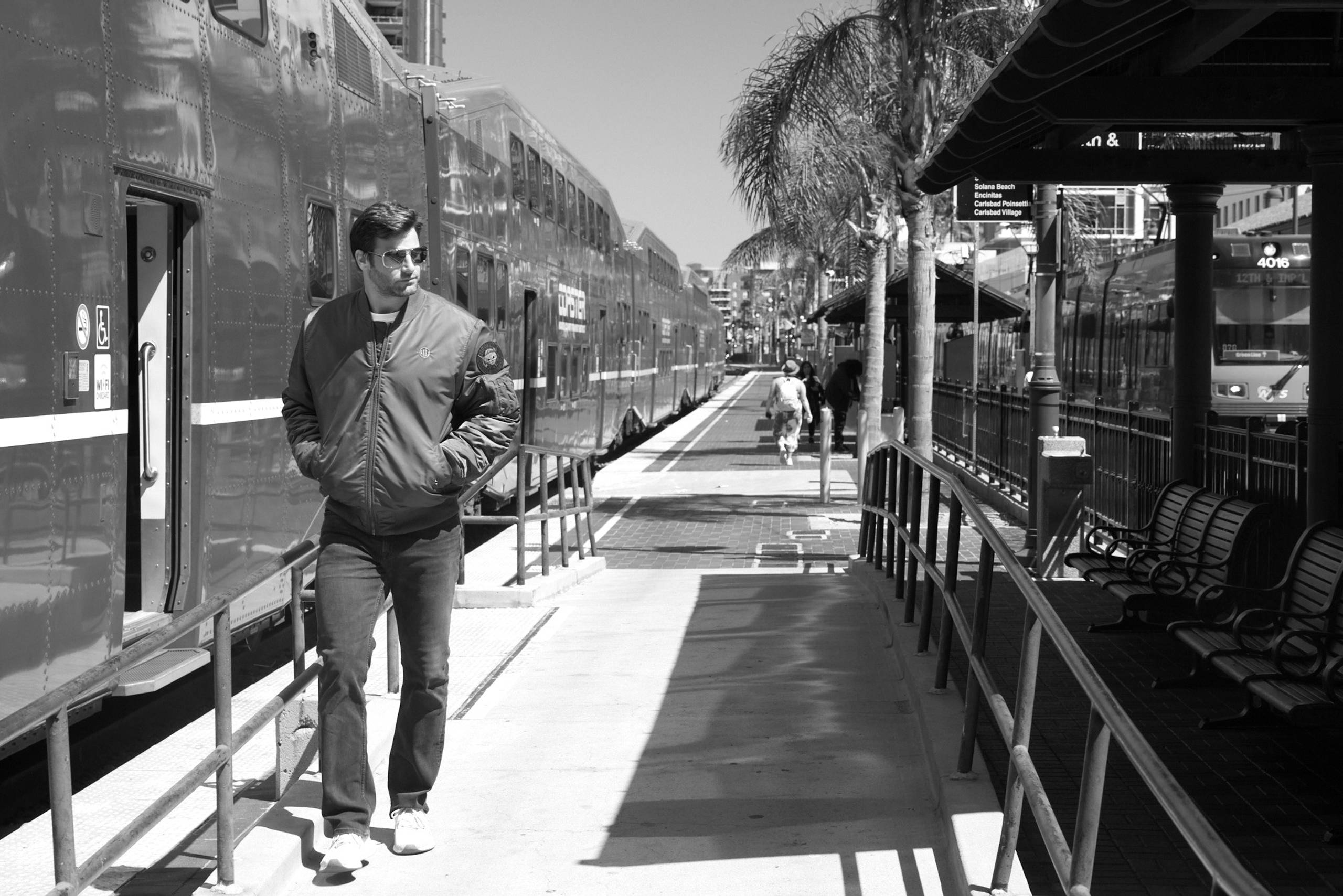 Man in bomber jacket walking past a train on a platform