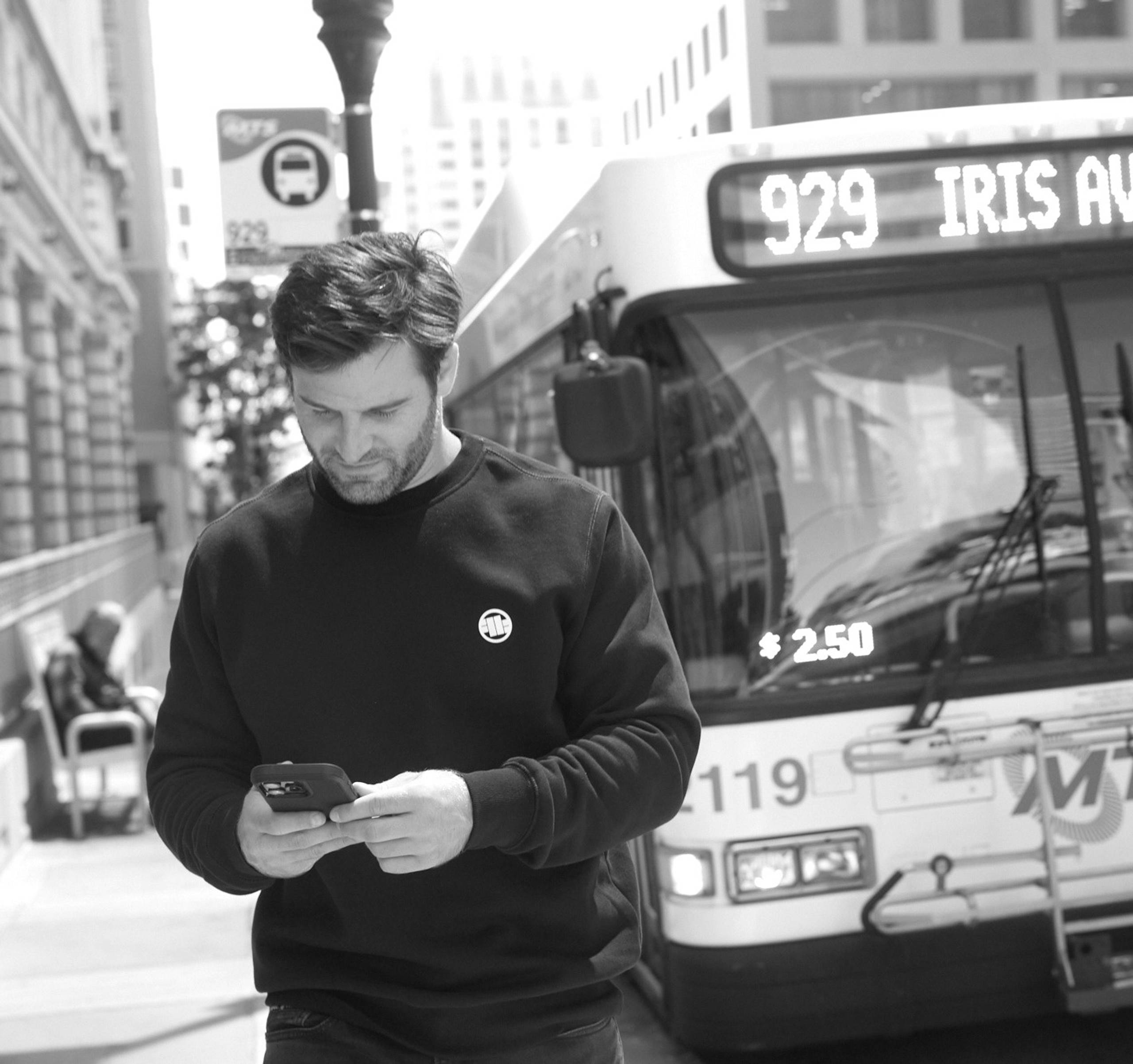 Man checking his phone in front of a city bus