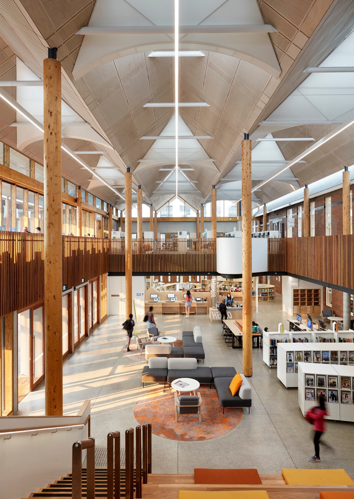 At Marrickville Library, double and triple-height spaces create a vast open foyer with warm wood tones, framing the retained walls of the original 1897 hospital.