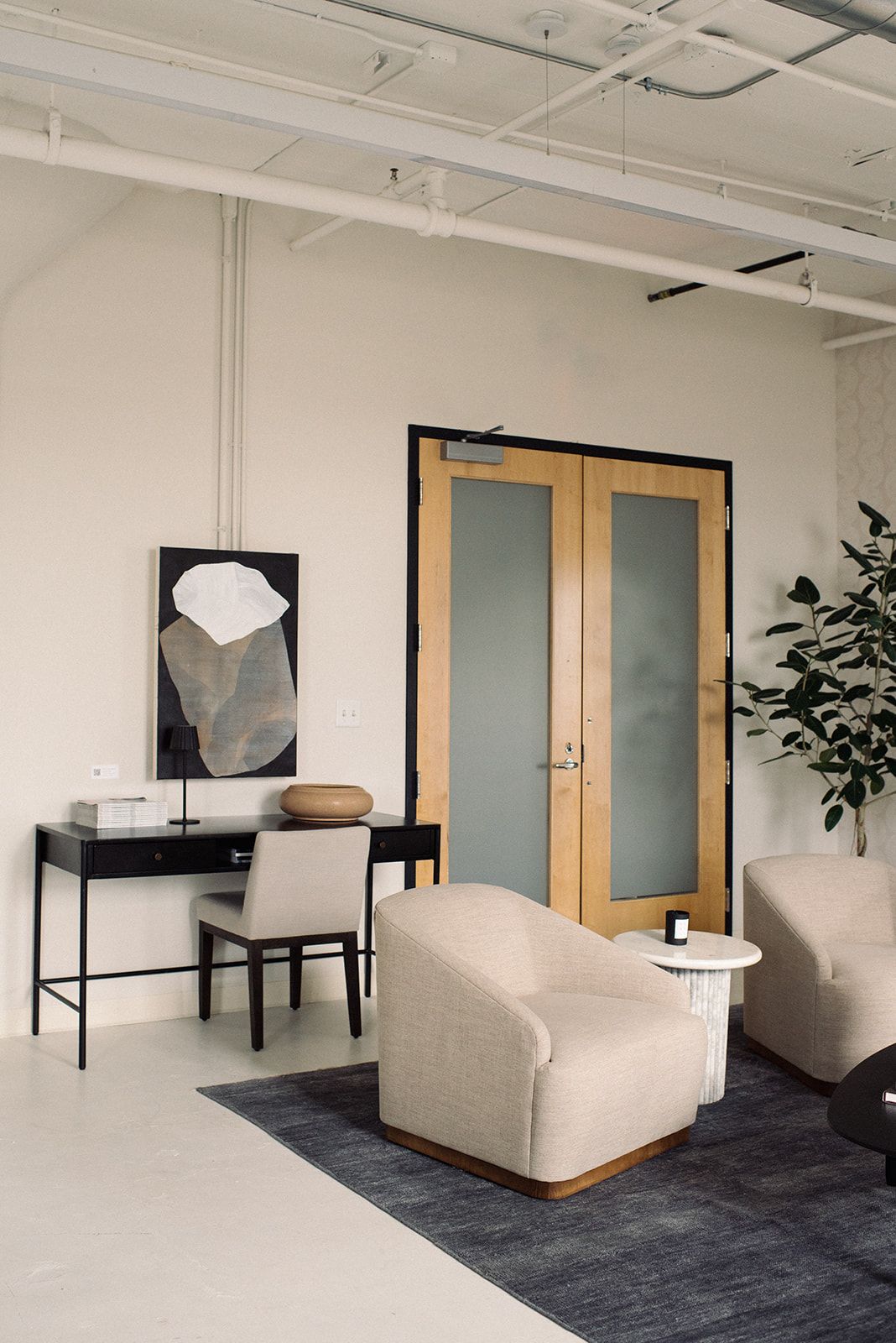 Lounge corner with a black console desk, abstract art, a beige swivel chair, a marble side table, and a charcoal rug.