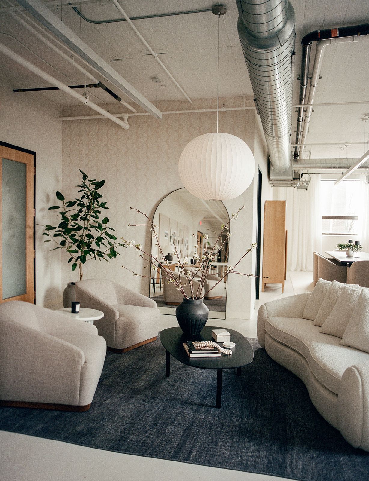 Lounge corner with patterned wallpaper, an arched mirror, beige swivel chairs, a marble side table, and a black oval coffee table.