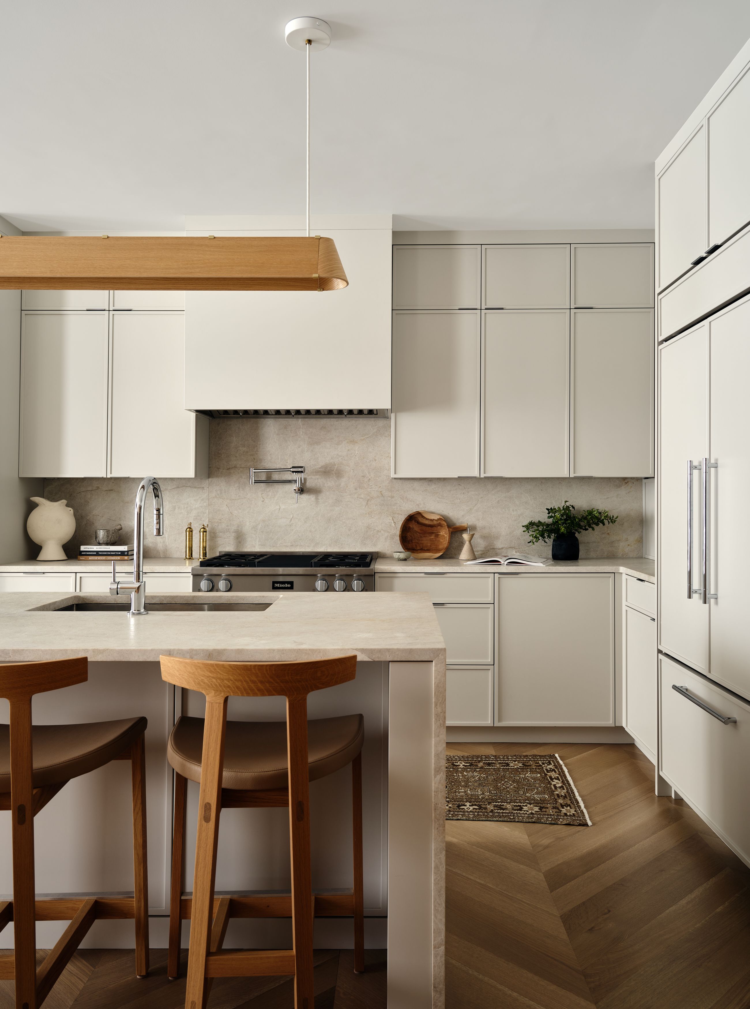 A bathroom with pale green cabinetry, a wood pendant light, stone backsplash, and leather-topped wood counter stools.