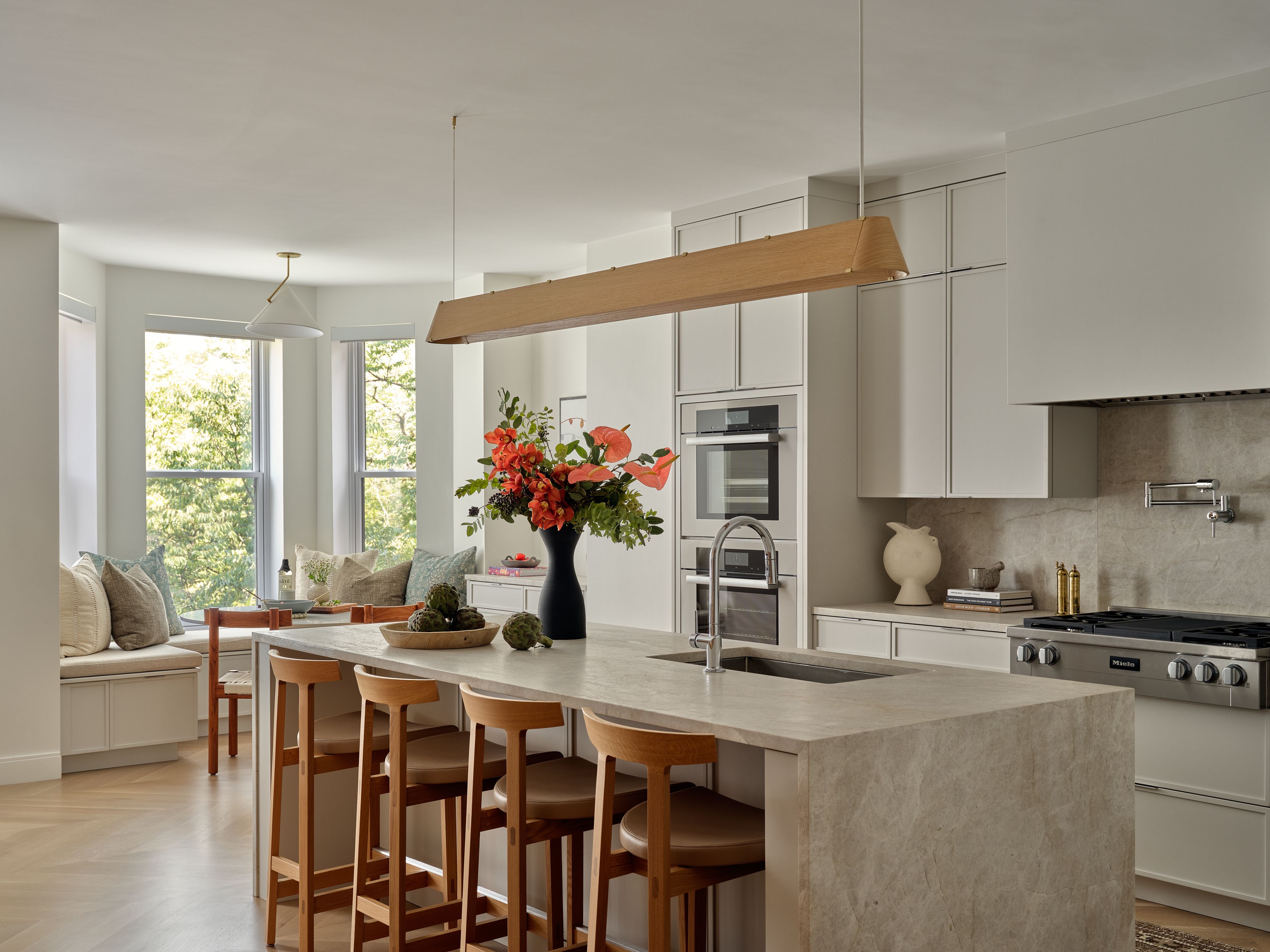 A kitchen with a wood-slat pendant light, a white waterfall marble island, and a bay-window breakfast nook.
