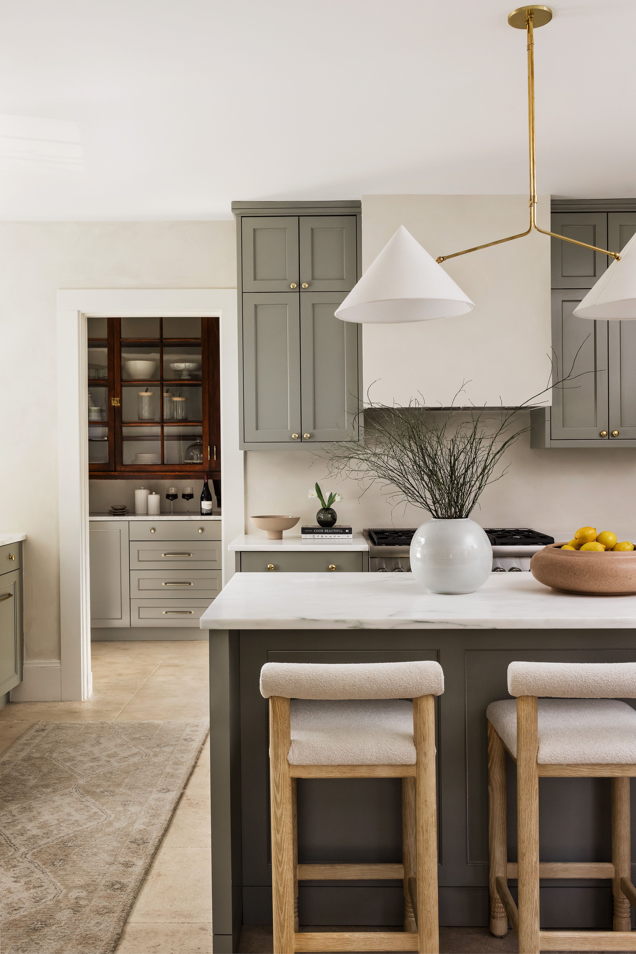 A kitchen island with a brass cone pendant light, a terracotta bowl of lemons, and a view into a wood-paneled butler's pantry.