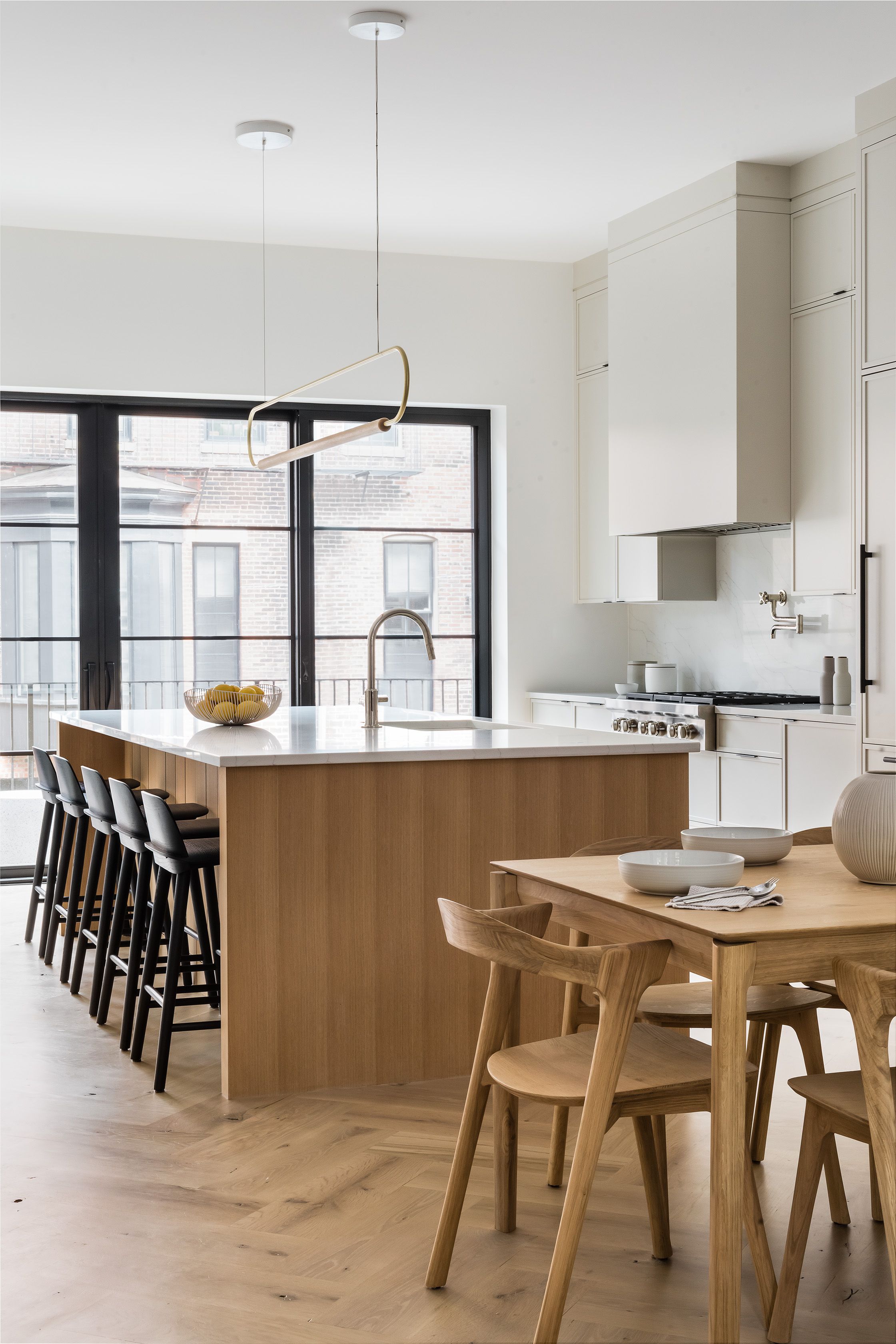 Kitchen with a wood island topped in white marble, a wire fruit basket, black-framed windows, and a pot-filler faucet over the range.