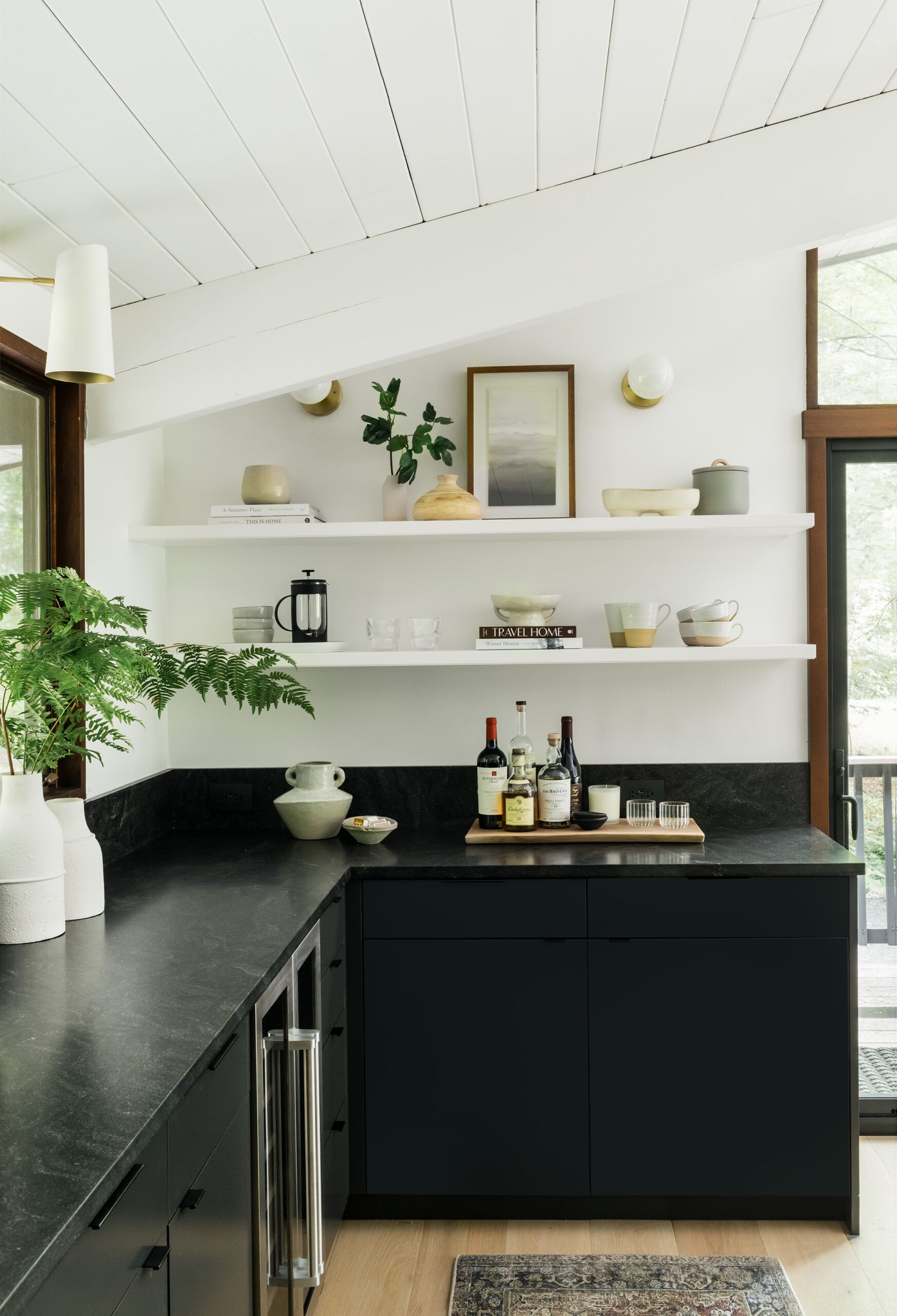 Floating shelves holding ceramics and books above a dark stone counter set with wine bottles and a bar tray.