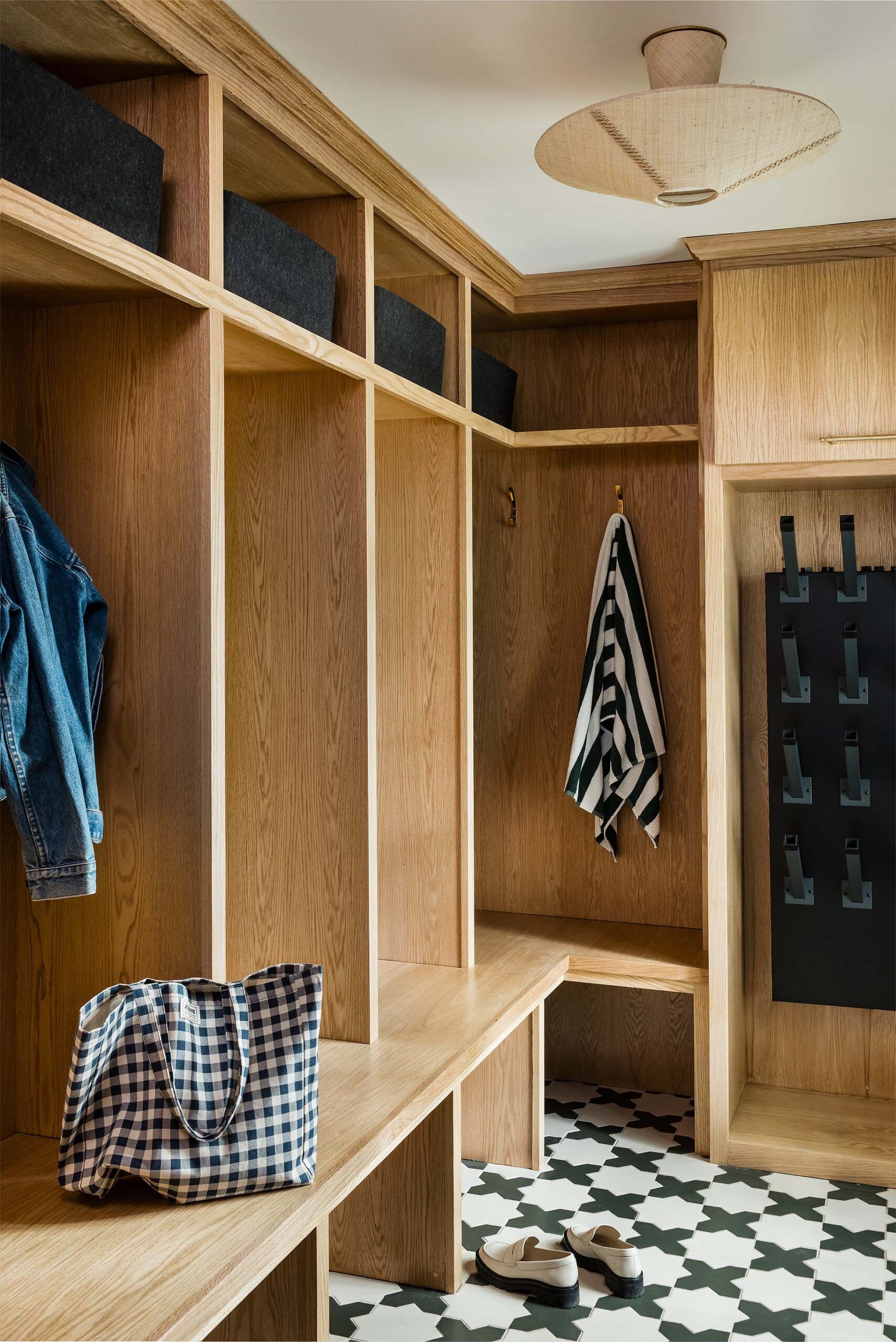 Mudroom with open oak lockers, felt storage bins, a woven disc ceiling light, and black-and-white cross-pattern floor tile.