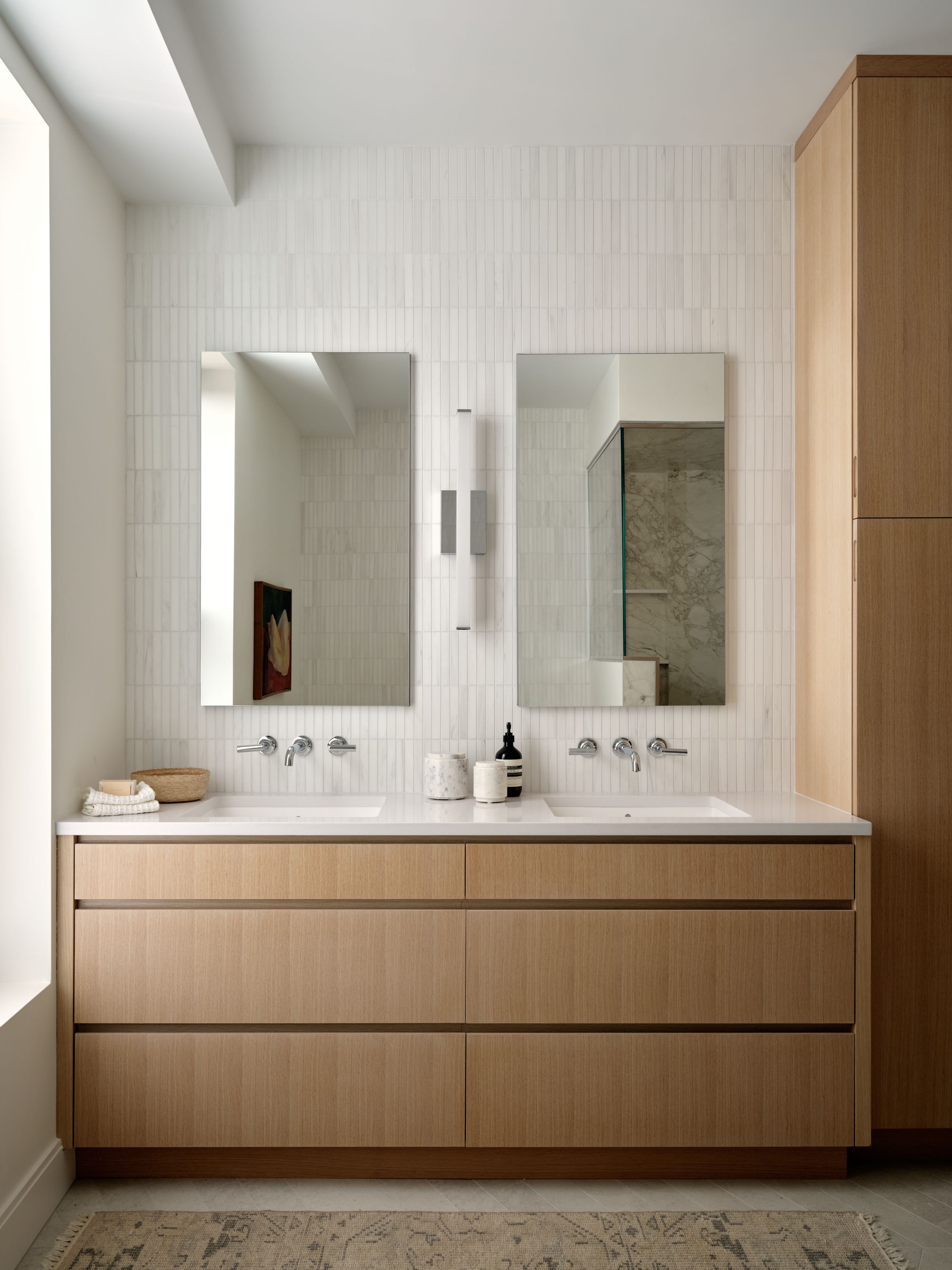 A primary bathroom double vanity with vertical ribbed marble tile, two rectangular mirrors, and a white oak cabinet base.